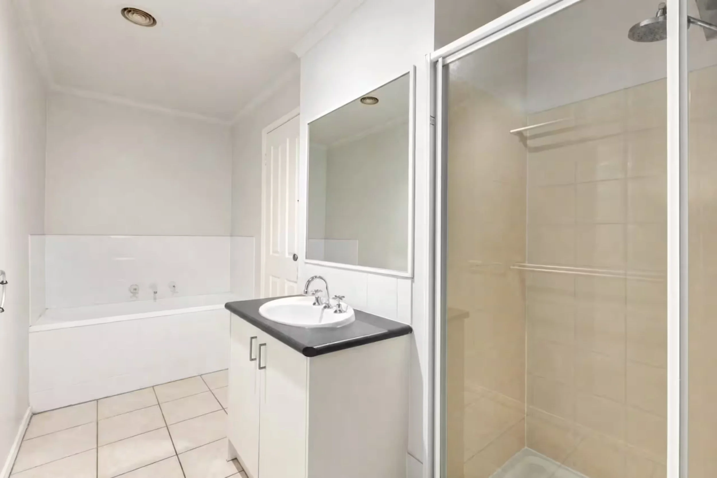Bathroom with a white bathtub, a white sink with a dark countertop, a mirror, and a glass shower enclosure with a built-in showerhead.
