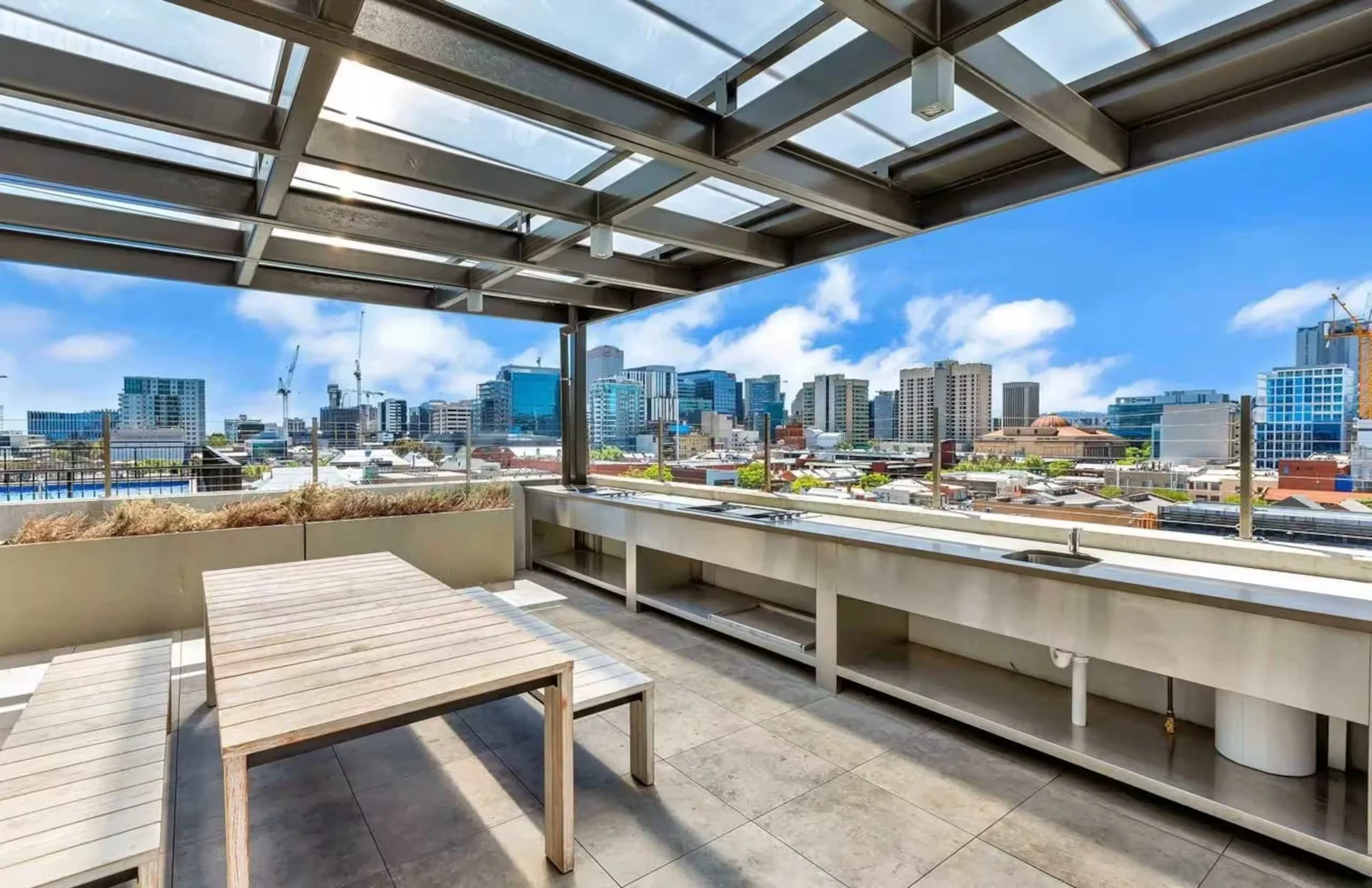 Under construction balcony or rooftop terrace with city skyline view in the background, blue sky, modern buildings, and construction cranes.