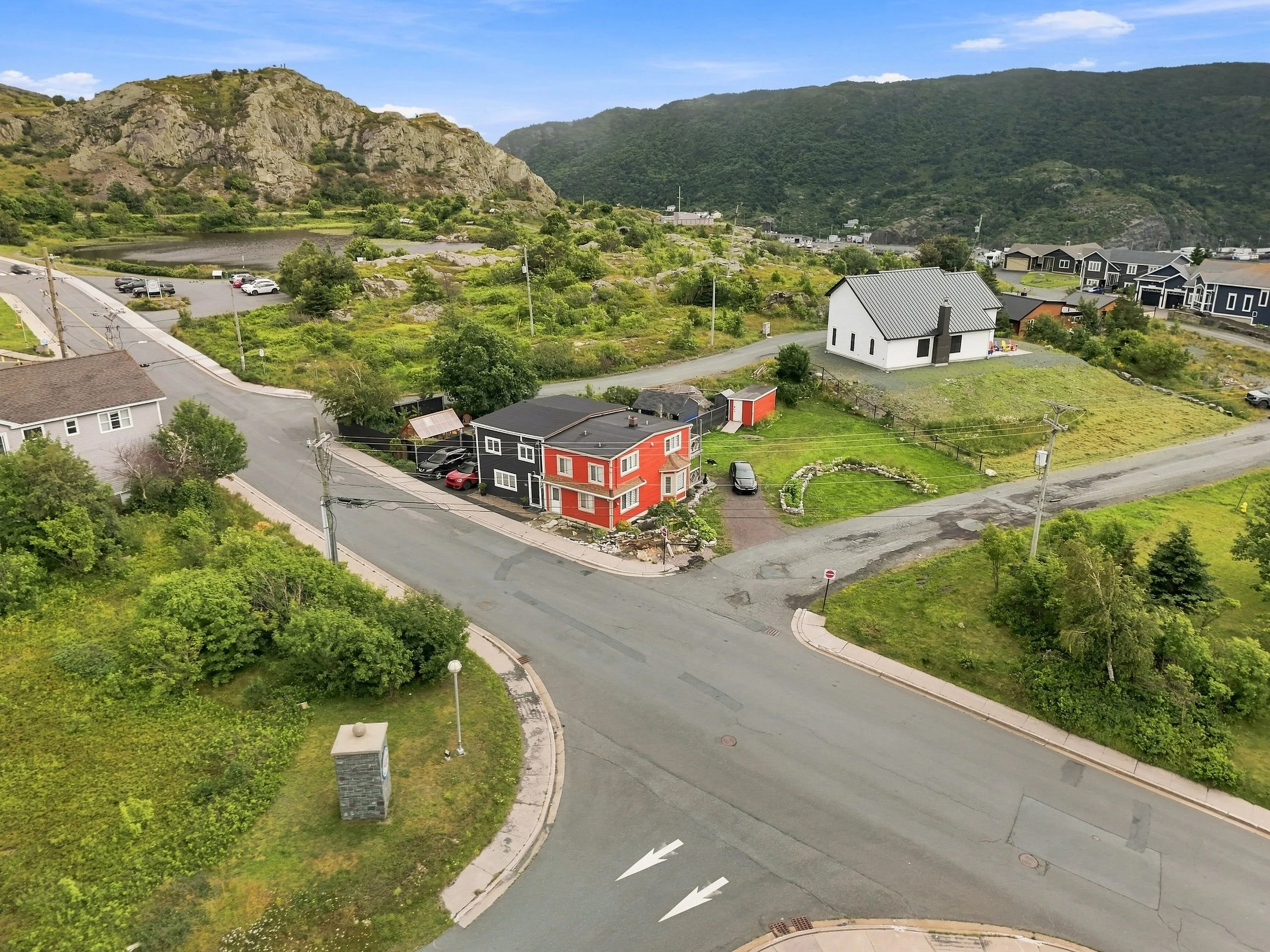 A small town with colorful houses, a parking lot, and a mountainous landscape in the background on a partly cloudy day.