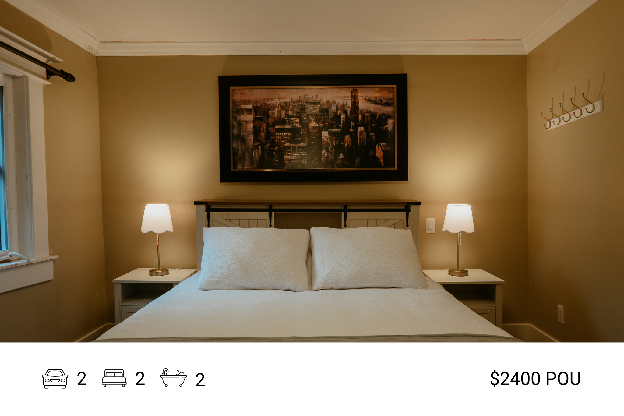 A bedroom with a bed, white bedding, and two pillows. Two nightstands with lamps flank the bed. A framed cityscape picture hangs above the headboard. The room has beige walls, a window on the left, and a coat rack on the right.