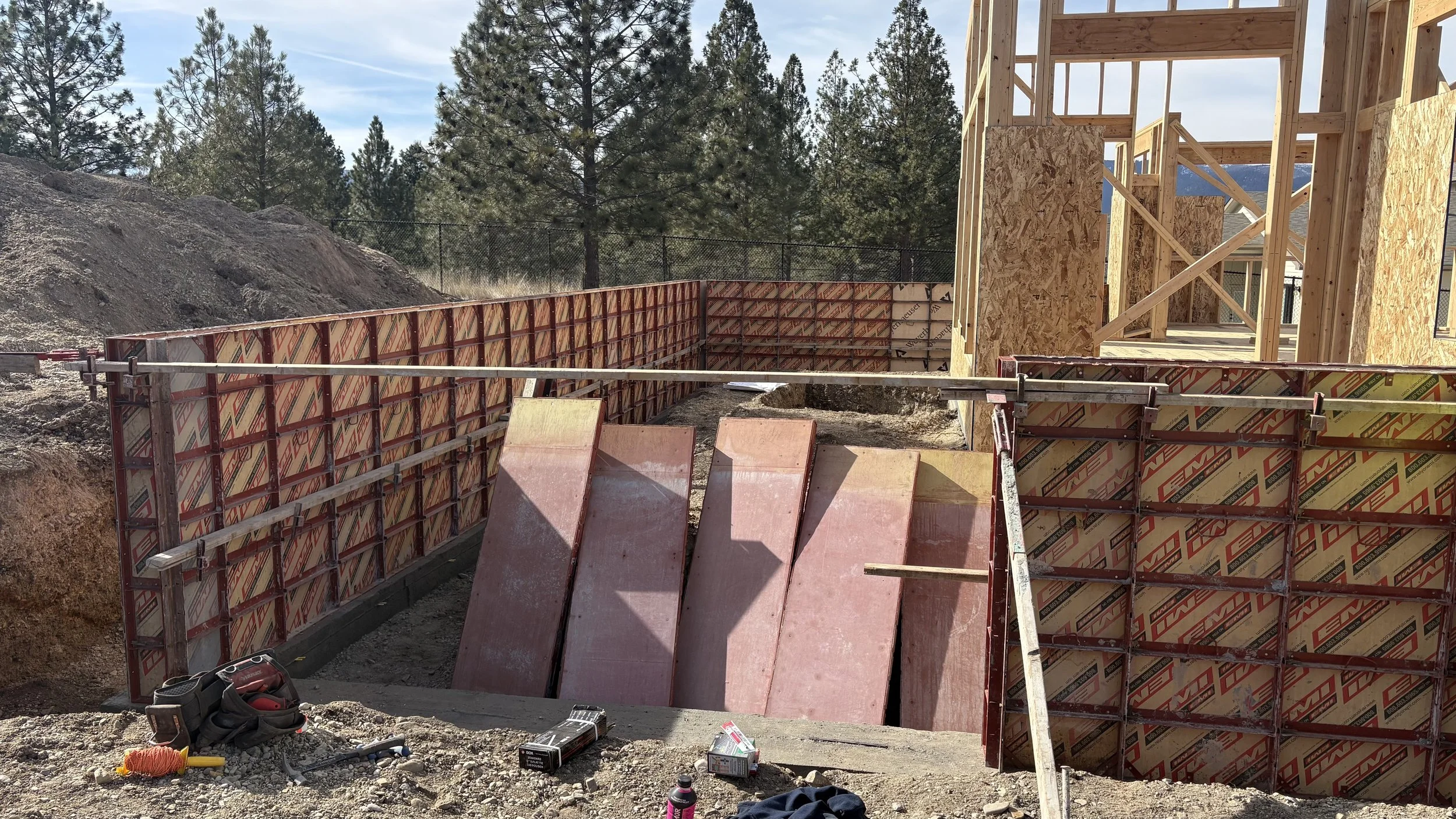 Construction site with wooden framing and concrete forms for a building foundation surrounded by dirt, trees, and nature.