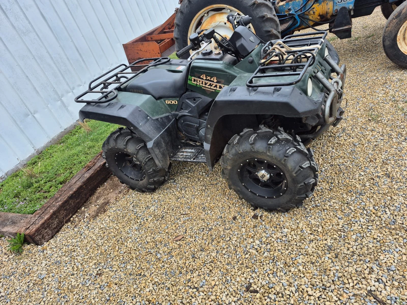 Green Yamaha four-wheel ATV with large tires parked on gravel next to a metal building wall.