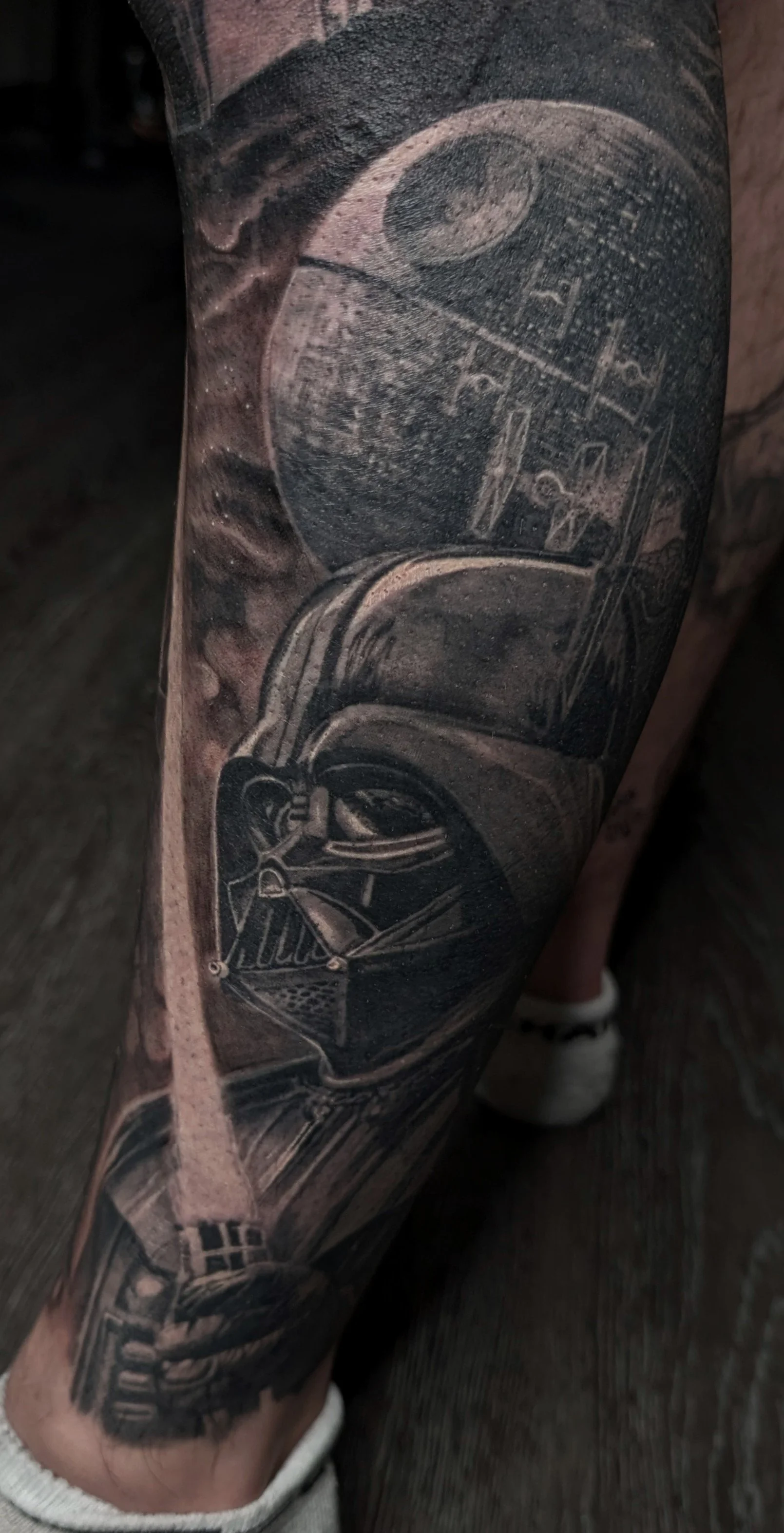 Tatouage en noir et blanc de Darth Vader et étoile noire de Star Wars sur la jambe.