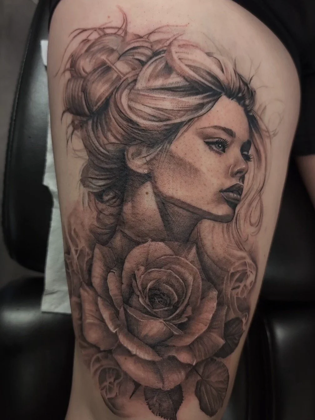 Tatouage réaliste d'une femme avec cheveux longs et une rose sous le visage, en noir et gris.