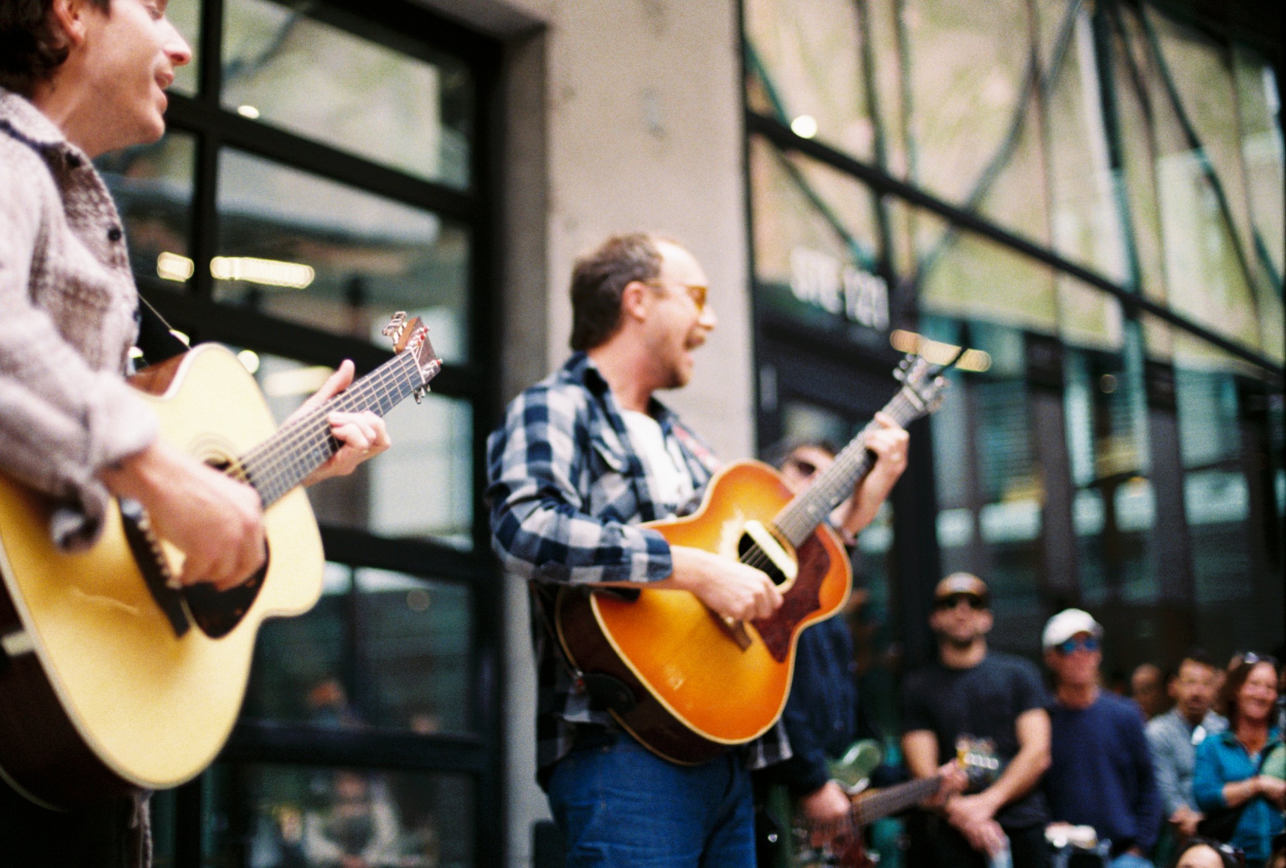 A group of musicians playing guitars during an outdoor performance with a crowd watching.