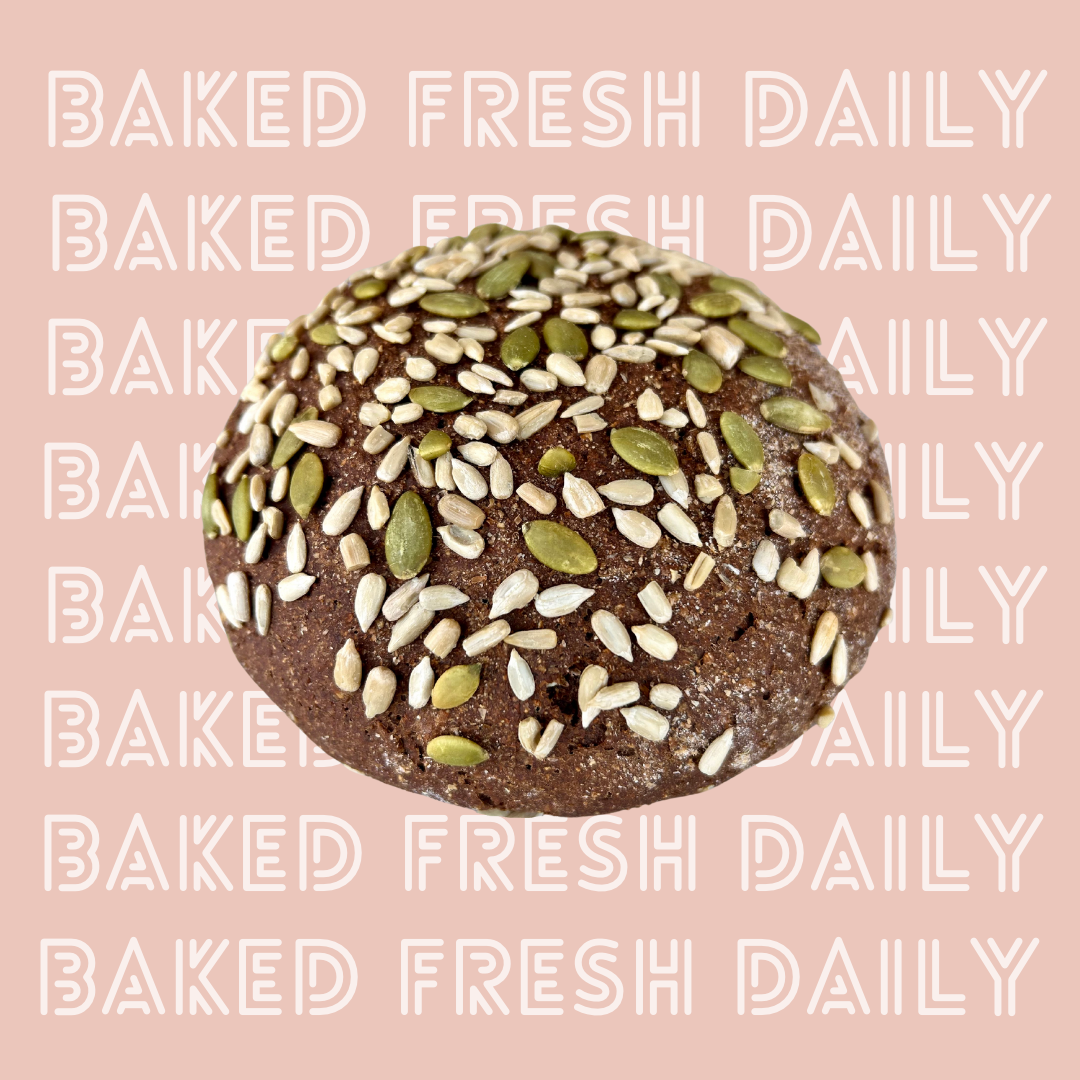 Close-up of a baked bread roll topped with sunflower and pumpkin seeds on a pink background with the text 'Baked Fresh Daily' repeated in a pattern.