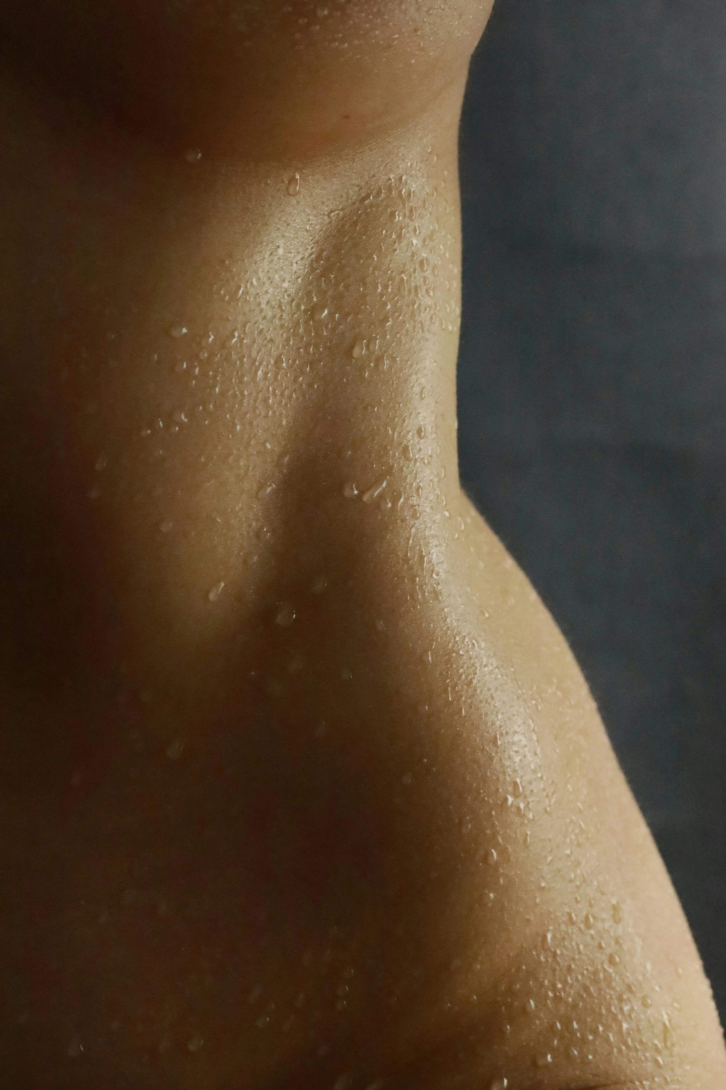 Close-up of a person's shoulder and neck with water droplets on skin against a black background.