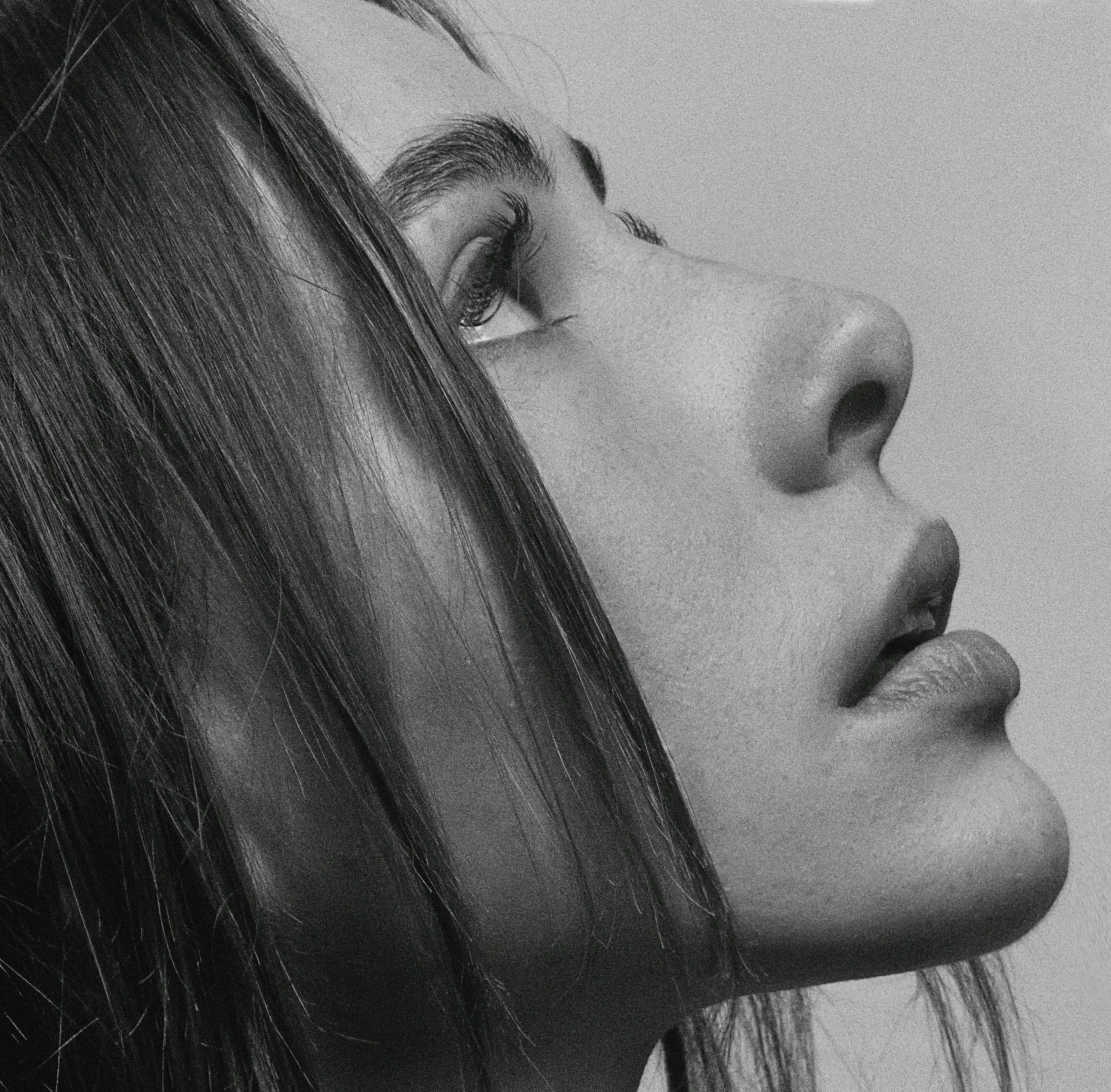Close-up black and white photo of a woman's face with long, dark hair, one eye visible and slightly closed.