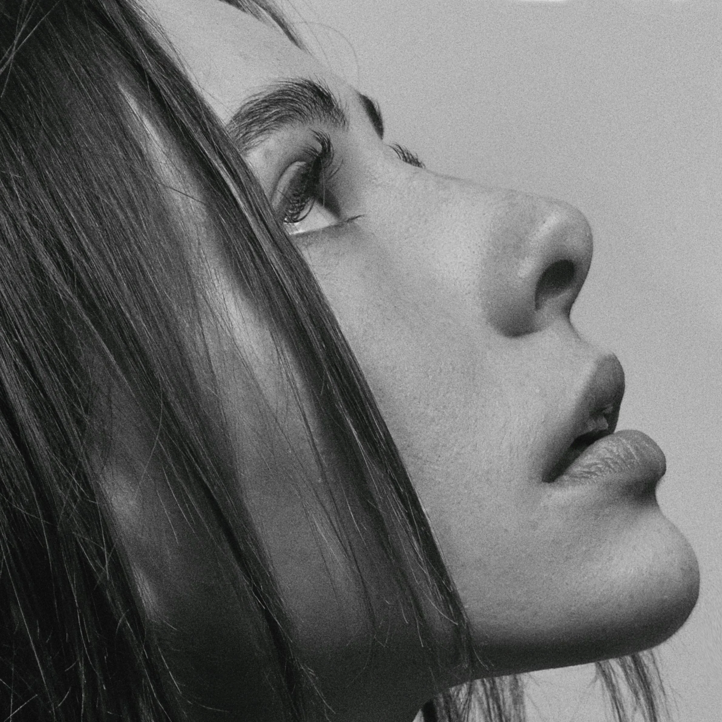 Close-up black and white photo of a woman's face focusing on her eye, eyebrow, and parts of her nose and forehead, with long dark hair partially covering her face.