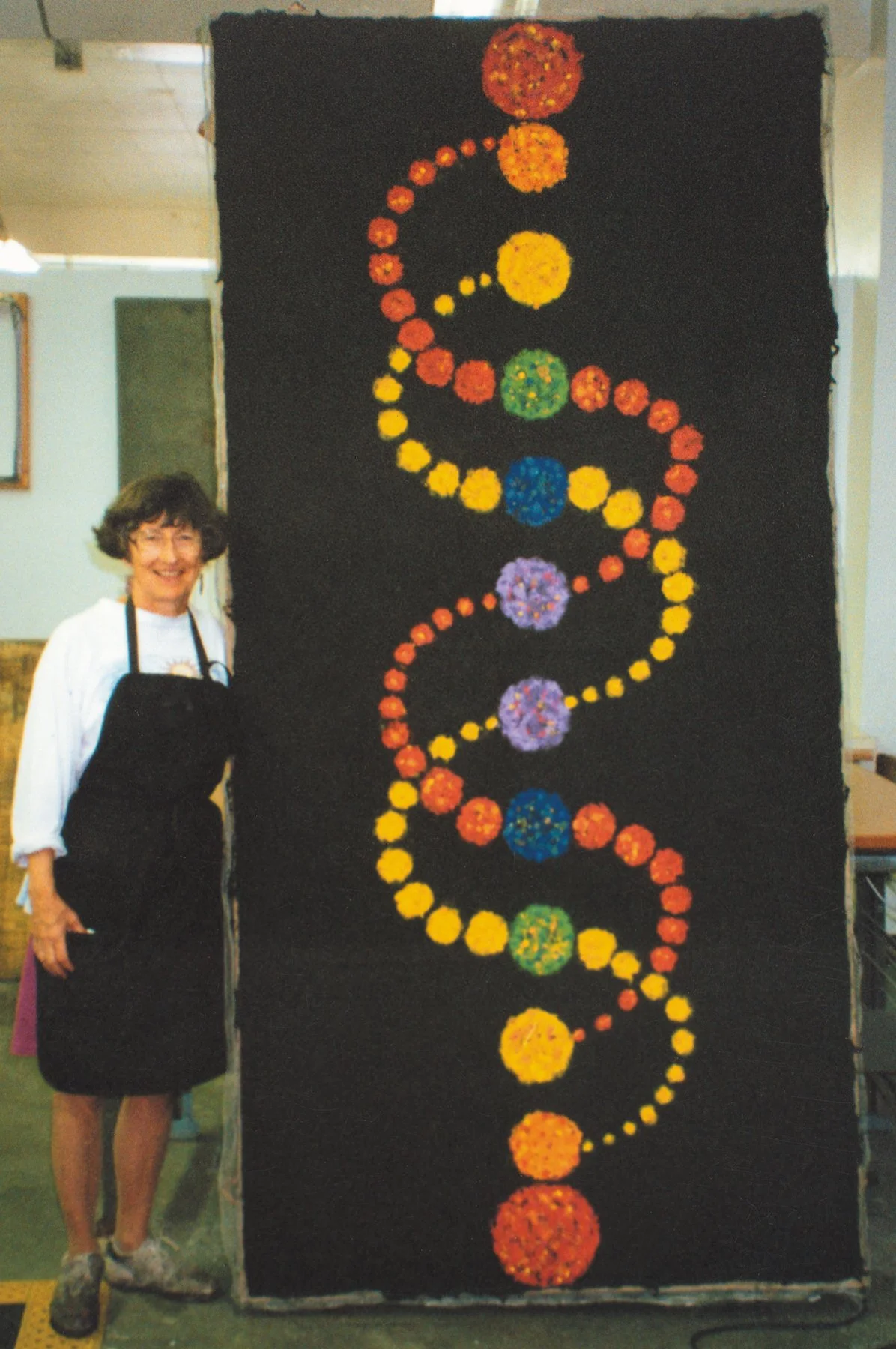 Lydia Ruyle standing next to a large black crop circle art piece made from handmade paper resembling a DNA double helix, at Columbia College Chicago.