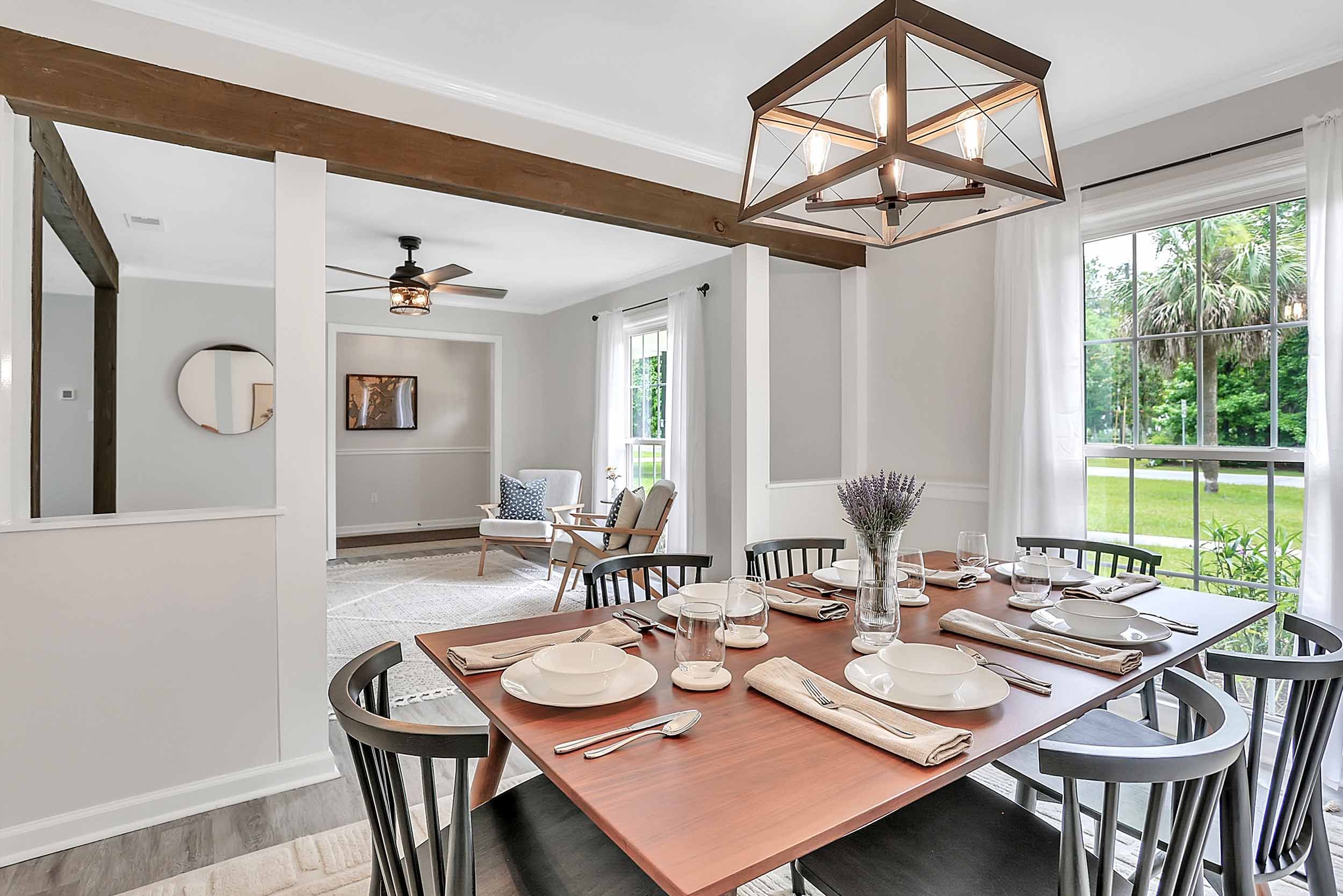 Alternate view of dining room inside Pomelo House vacation rental, open into sitting room, with oversized windows looking out to tree-lined streets of family-friendly neighborhood on Wilmington Island