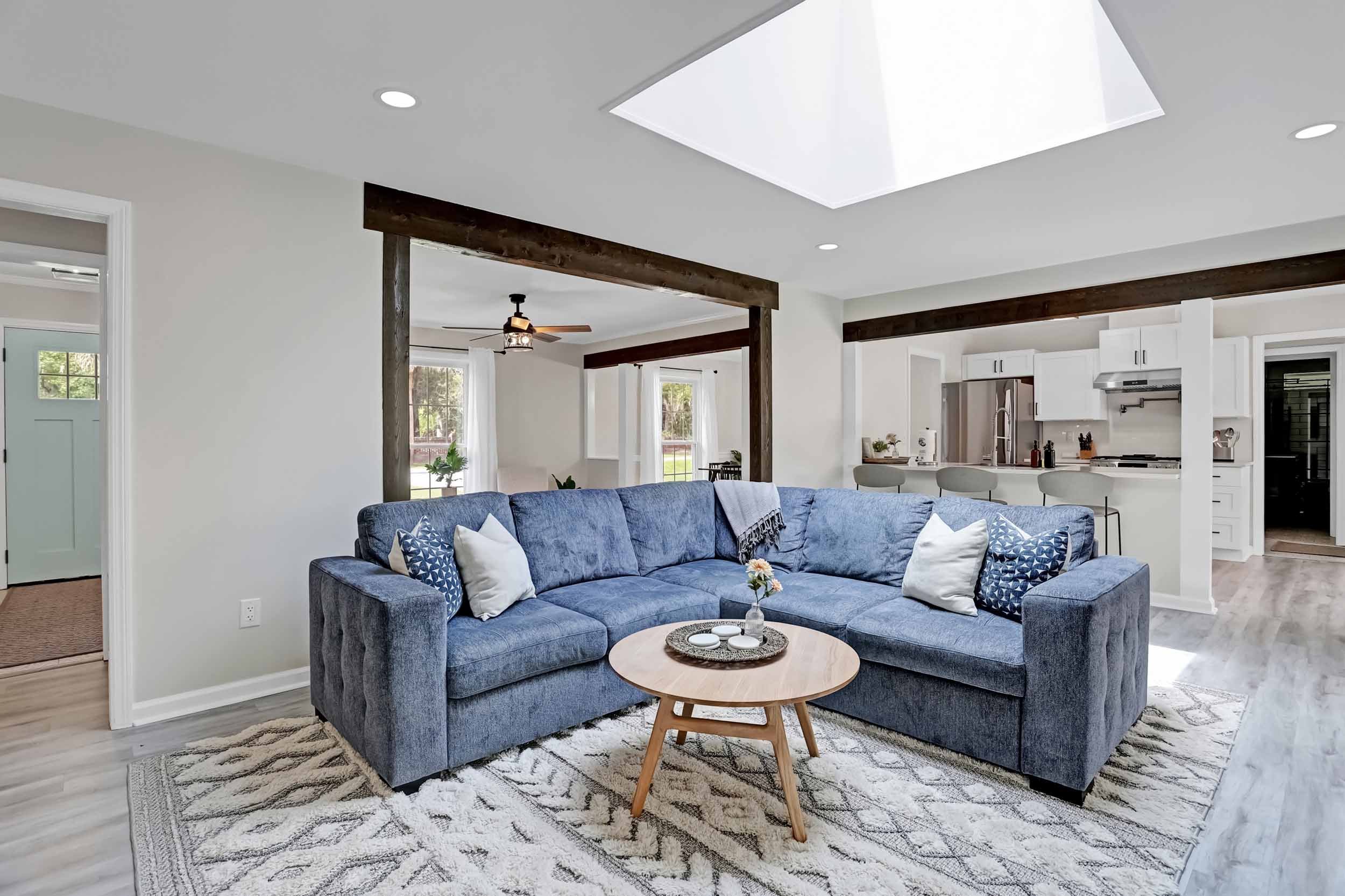Bright living room of Pomelo House Savannah vacation home with large skylight, spacious sectional with pillows and blanket, white oak coffee table, exposed wood beams, open to kitchen and view of pool