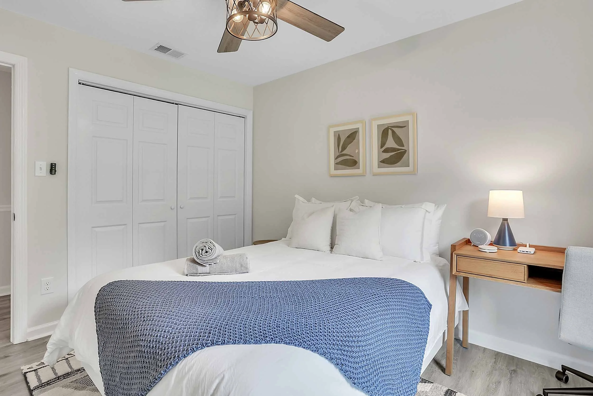 Alternate view of second queen bedroom at Pomelo House on Wilmington Island, near Tybee and downtown, showing luxurious bedding, desk with office chair, lamp, closet, fan, open door to hall with bath