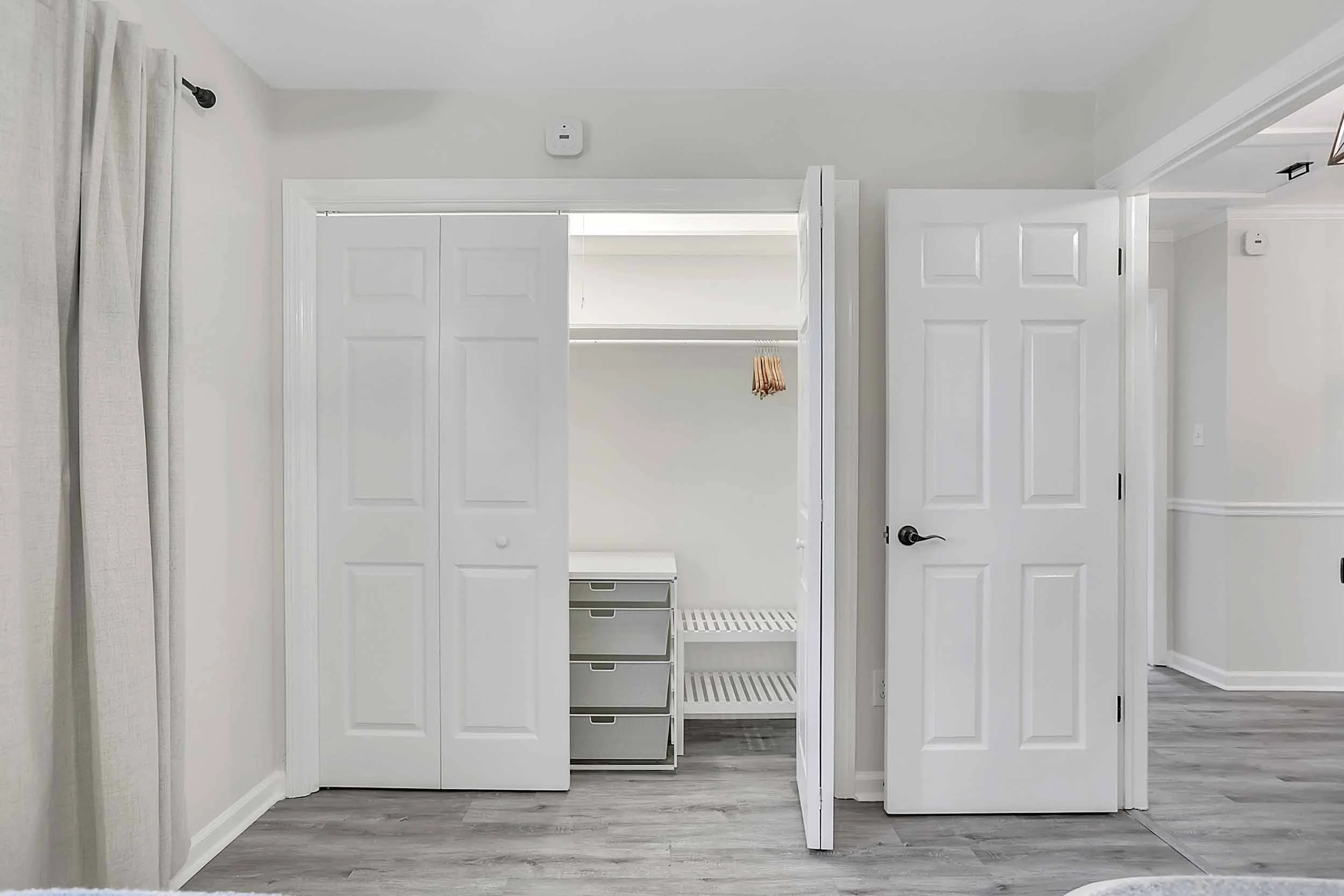 Alternate view of dual-twin bedroom at Pomelo House vacation rental showing open closet, hanging rod, Elfa drawers, shoe shelf, blackout curtains, gray vinyl flooring, open door to hallway bathroom