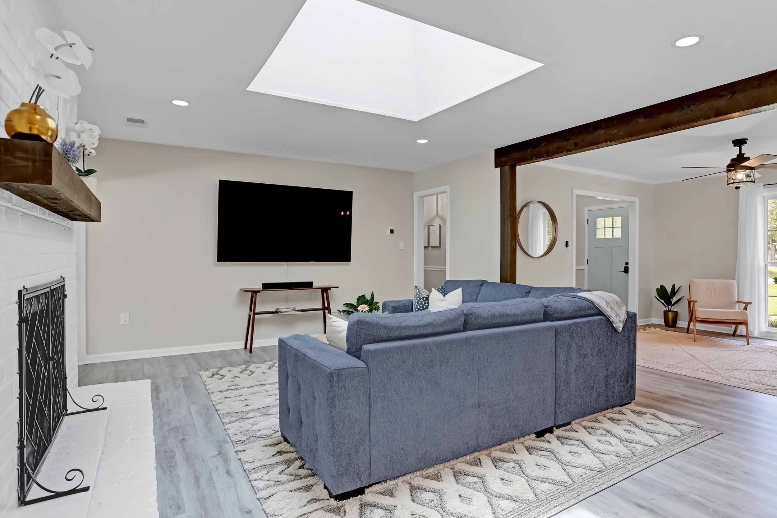 Living room of Pomelo House vacation rental in Savannah, GA showing open-concept center of home with large skylight, cozy sofa, exposed wood beams, 77” TV, and view of sitting room and entryway