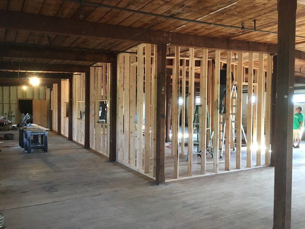 Interior of a building under construction with exposed wooden framing and workers installing walls.