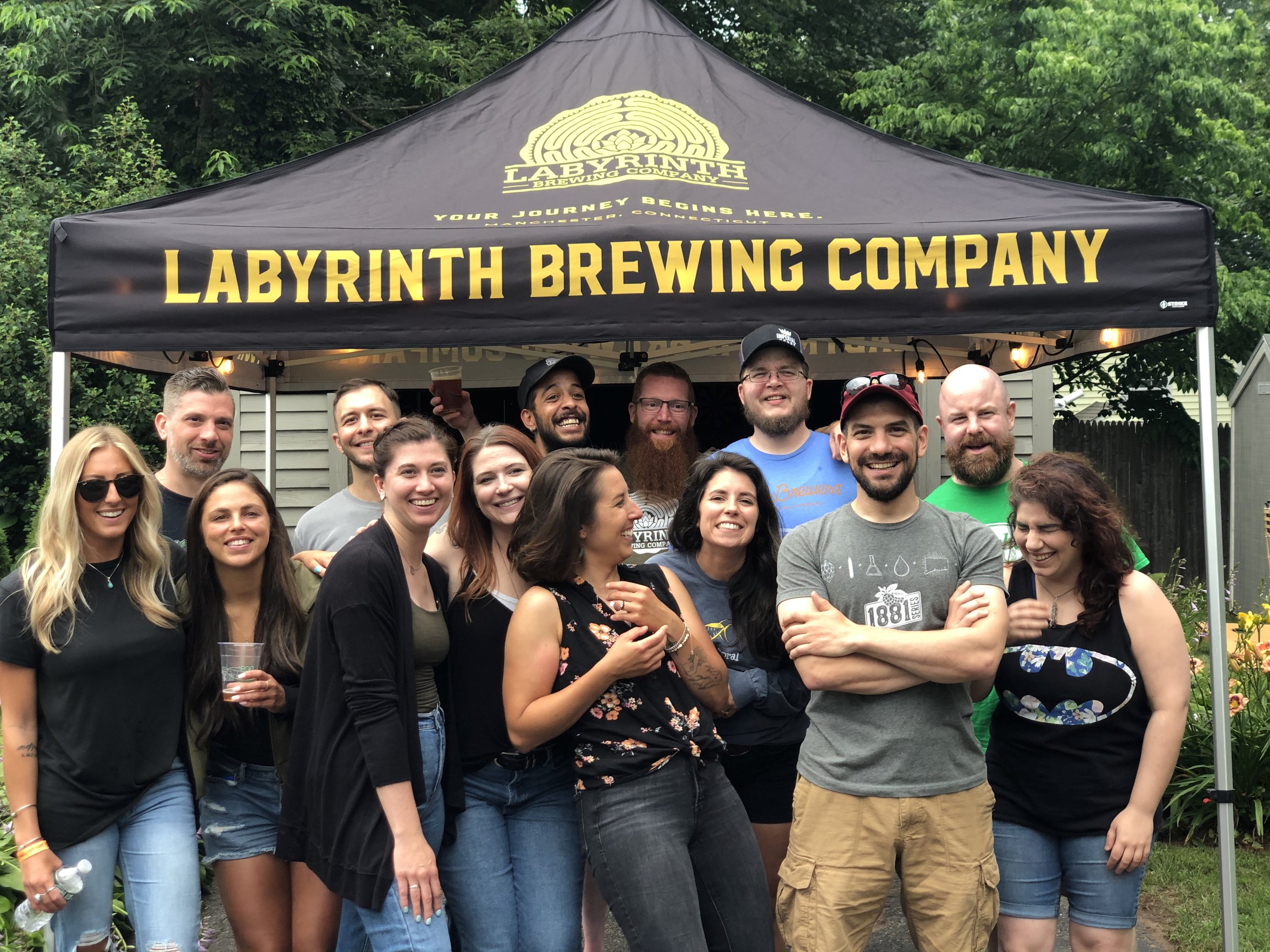 Group of people smiling and posing in front of a labyrinth brewing company tent during an outdoor event.