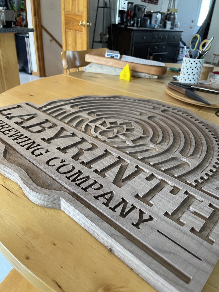 Wooden sign with the words 'ABINGTON THEATRE & READING COMPANY' cut out in capital letters, placed on a wooden table in a kitchen or workshop setting.