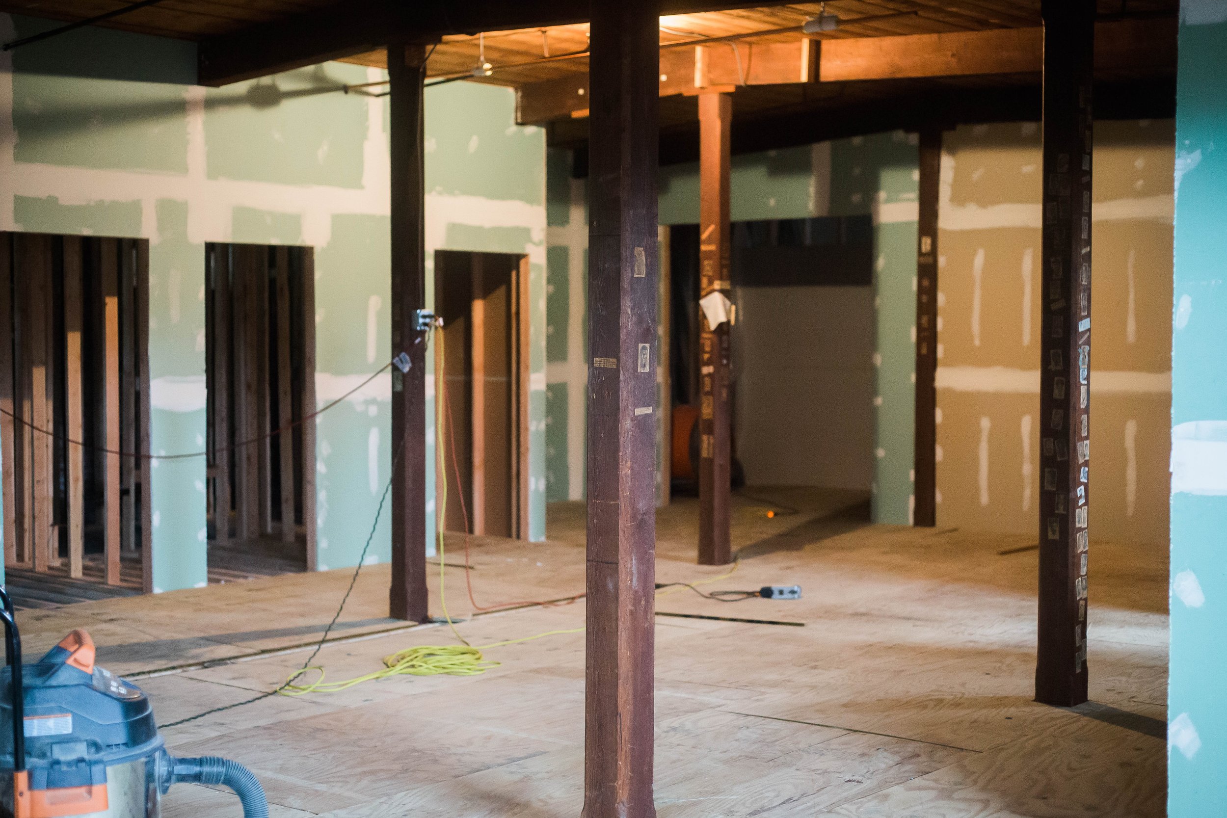 Interior of a building under construction with exposed green drywall, wooden framing, and partially finished walls.