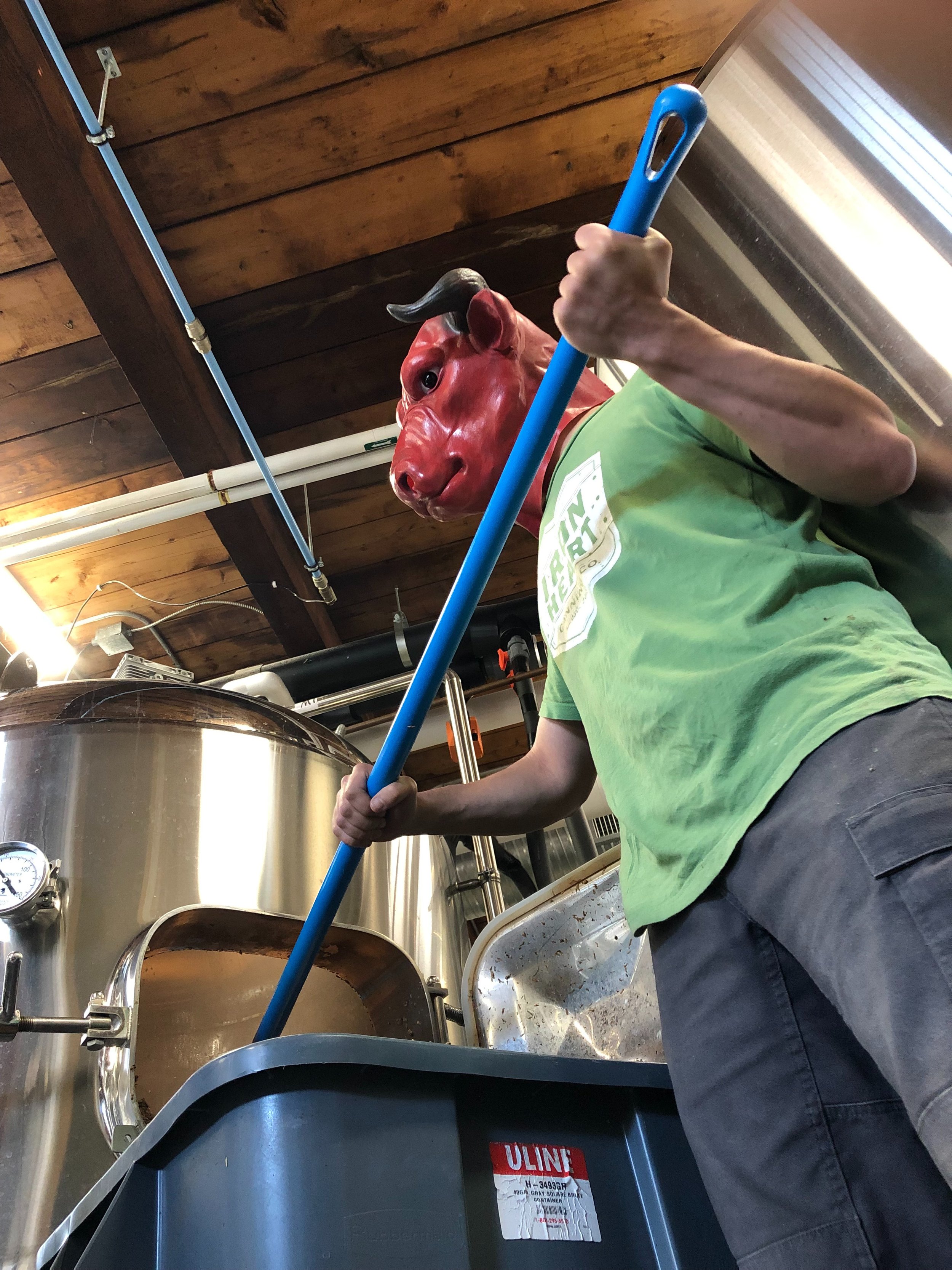 Person wearing a red devil mask stirring a brew in a brewery.