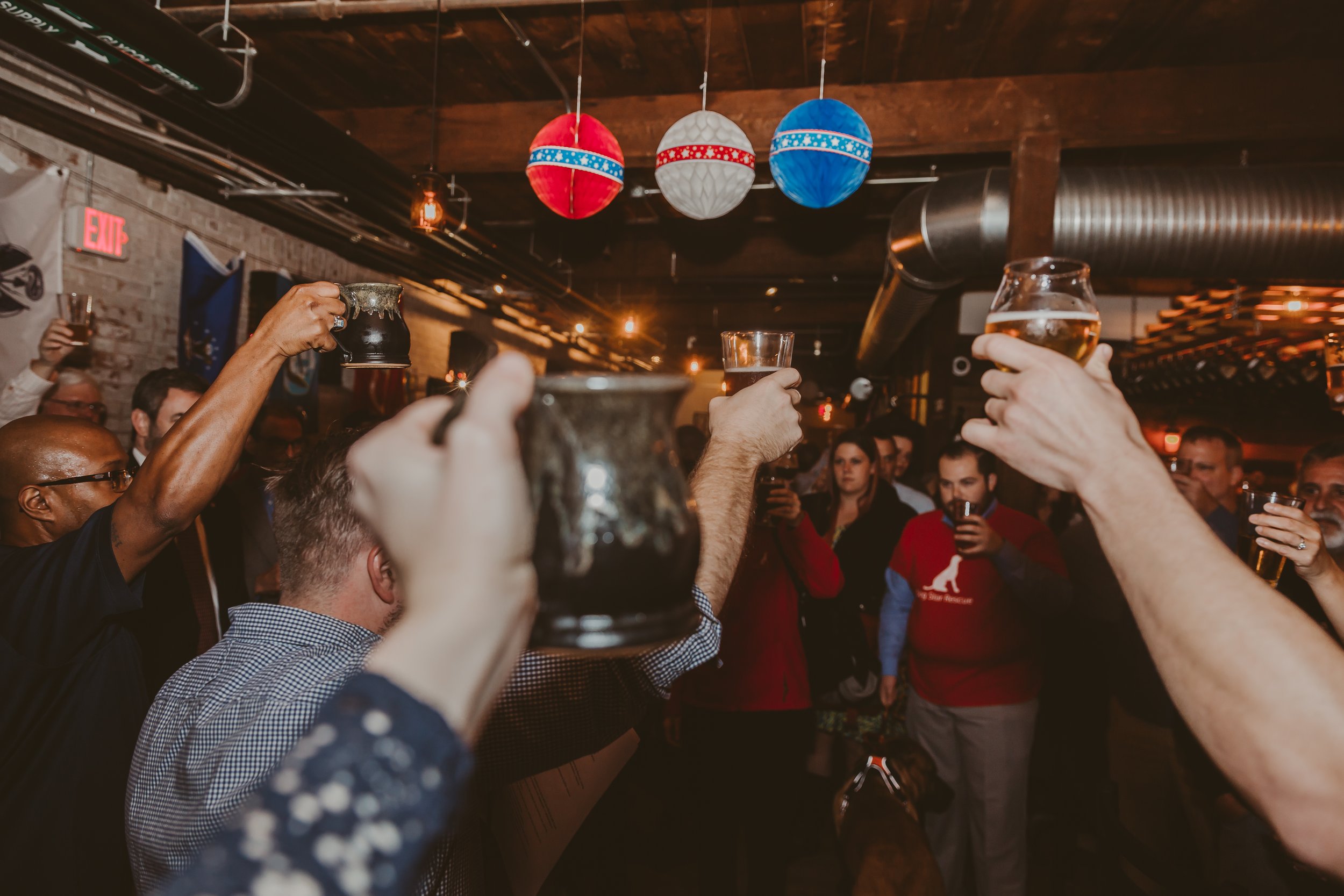 People in a bar raising their glasses in a toast, with Christmas decorations hanging from the ceiling.