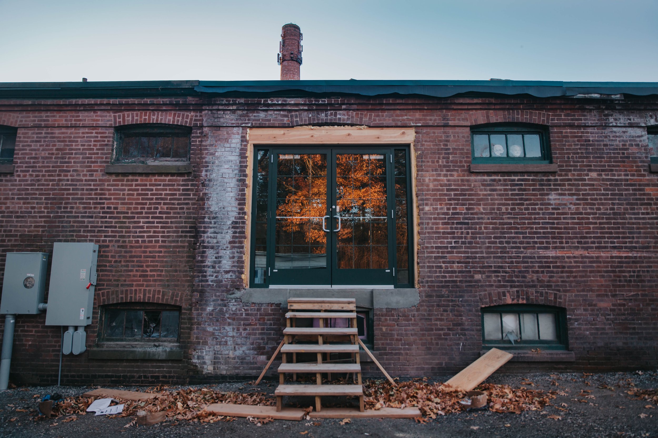 Back of a brick building with a new glass door framed in wood, a small staircase, and construction materials on the ground.