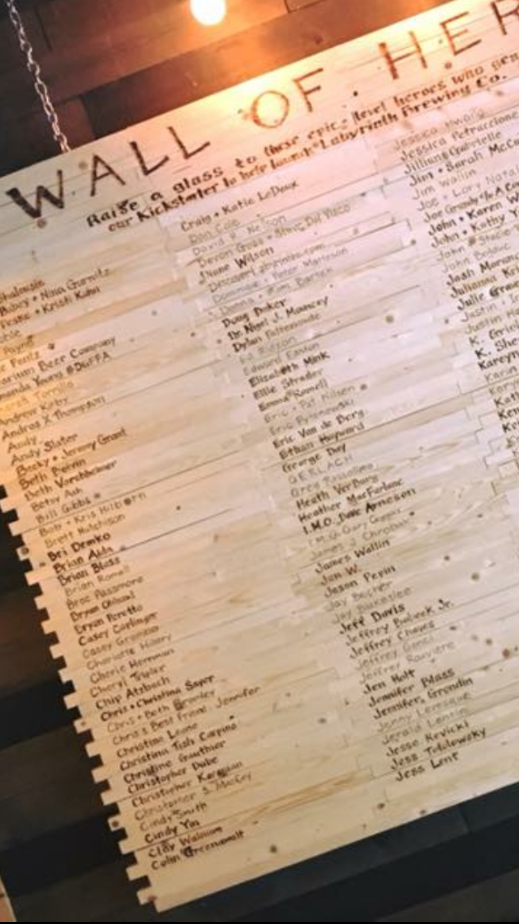 Wooden wall with a sign titled 'Wall of Heroes' and a list of names underneath.