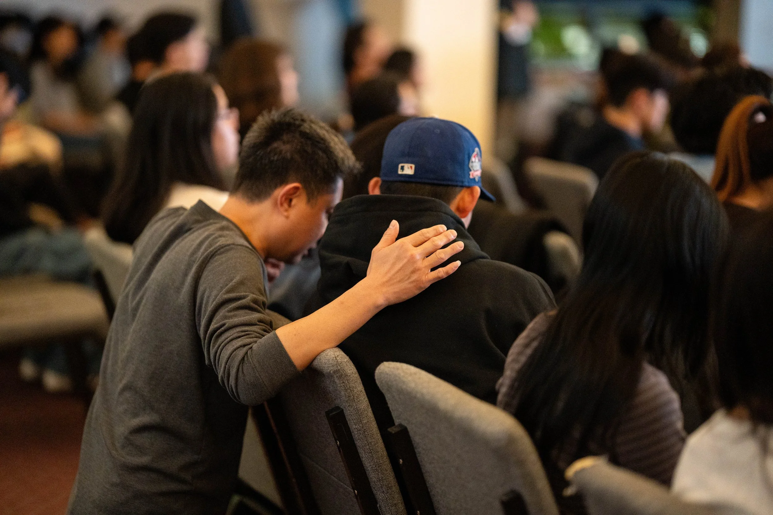 A brother praying for another brother. His hand is on the brother's back showing comfort and care.