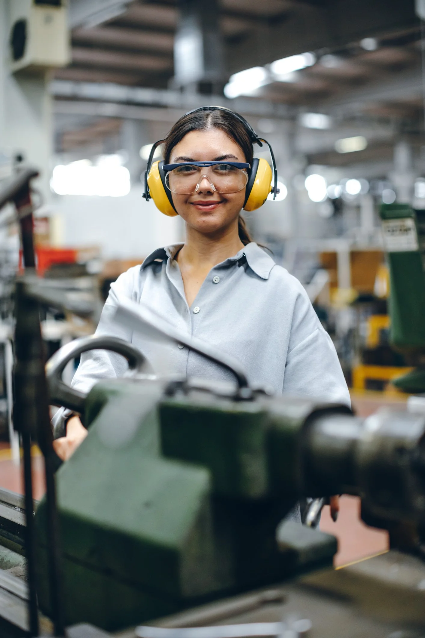 A woman wearing safety goggles and yellow ear protection in a workshop, with machinery. She is about to have audiometric testing in the Central Coast, NSW.