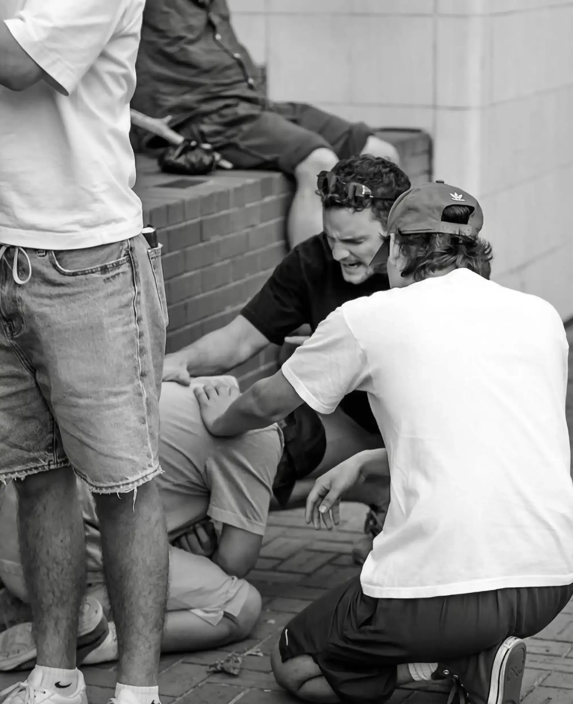 People assisting a person who appears to be injured or unwell on the ground, with others surrounding and helping.