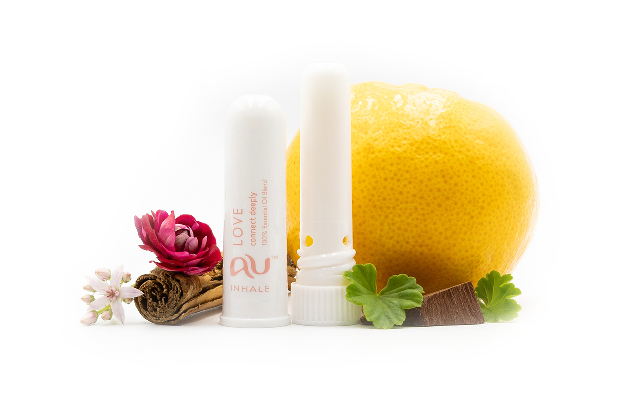 The Love Essential Oil inhaler is arranged on a white background, the cap has been taken off and it sitting next to the inhaler, surrounded by its ingredients - fruit, herbs and spices.
