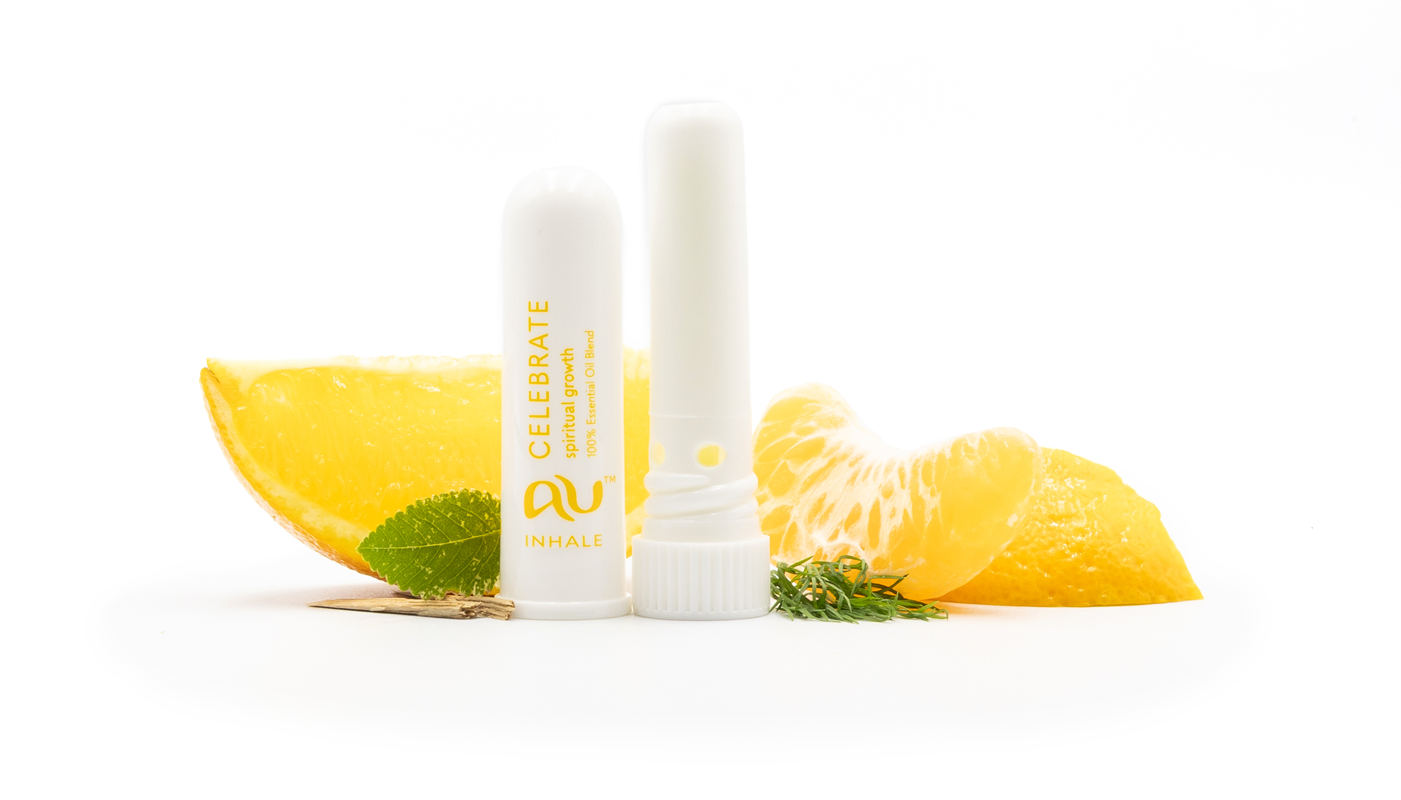 The Celebrate Essential Oil inhaler is arranged on a white background, with its cap off and sitting adjacent, surrounded by its ingredients - fruit, herbs and spices.