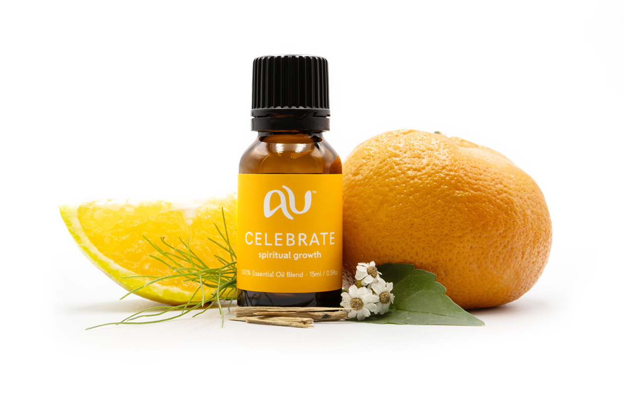 The Celebrate Essential Oil Blend bottle is arranged on a white background surrounded by its ingredients - fruit, herbs and spices.