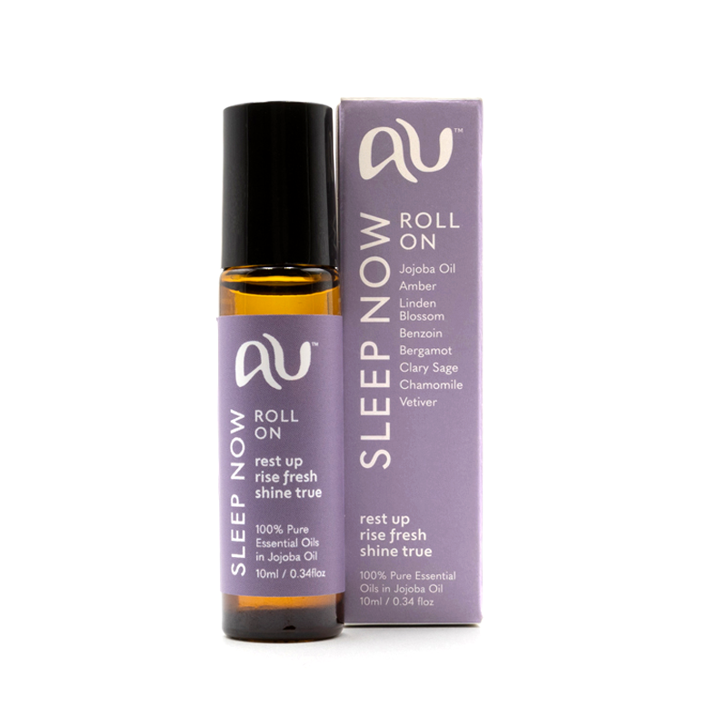 The Sleep Now Roll On is sitting on a white background next to its box. The bottle is long and slender with a lilac label and black lid. The box is lilac with white graphics.