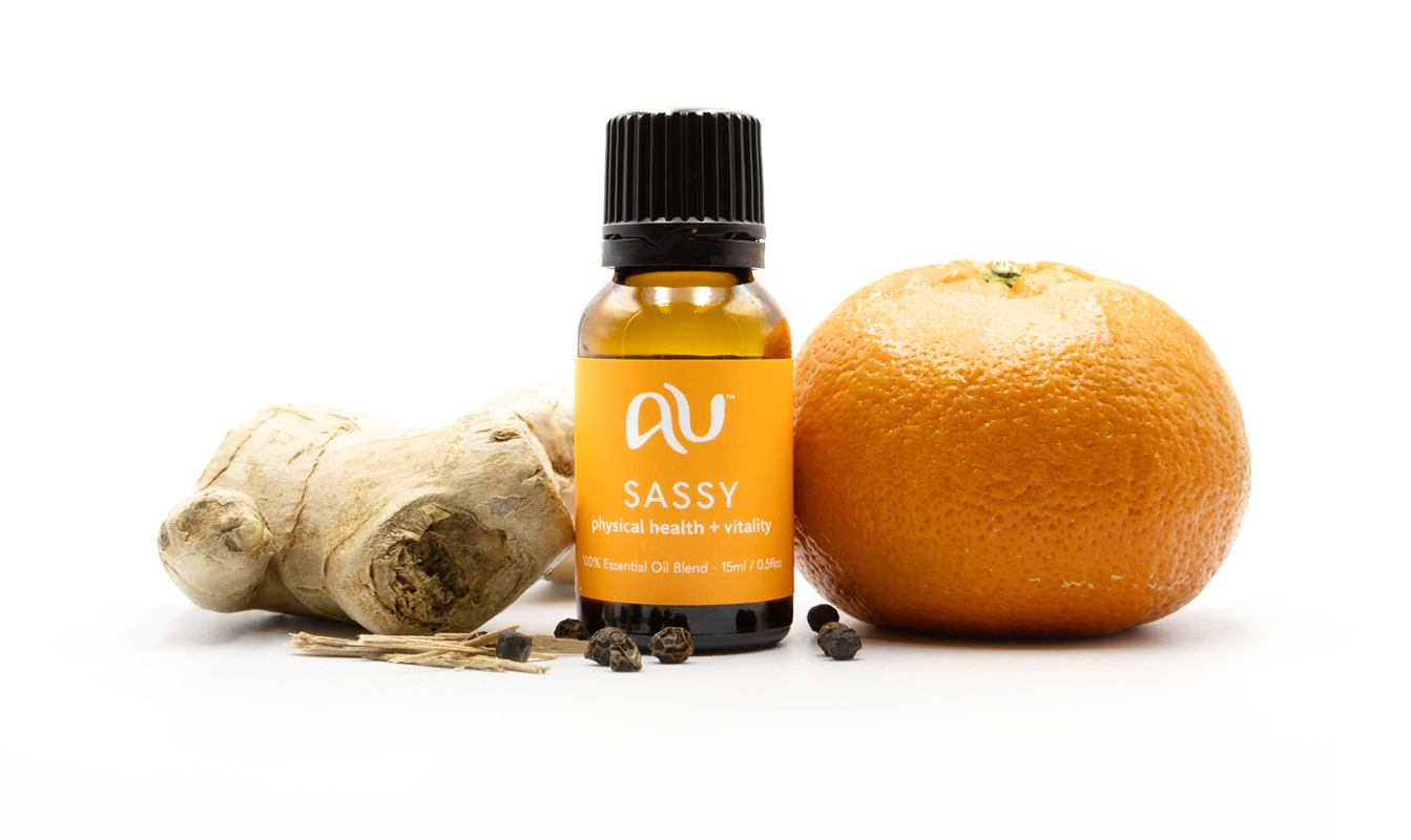 The Sassy Essential Oil Blend bottle is arranged on a white background surrounded by its ingredients - fruit, herbs and spices.
