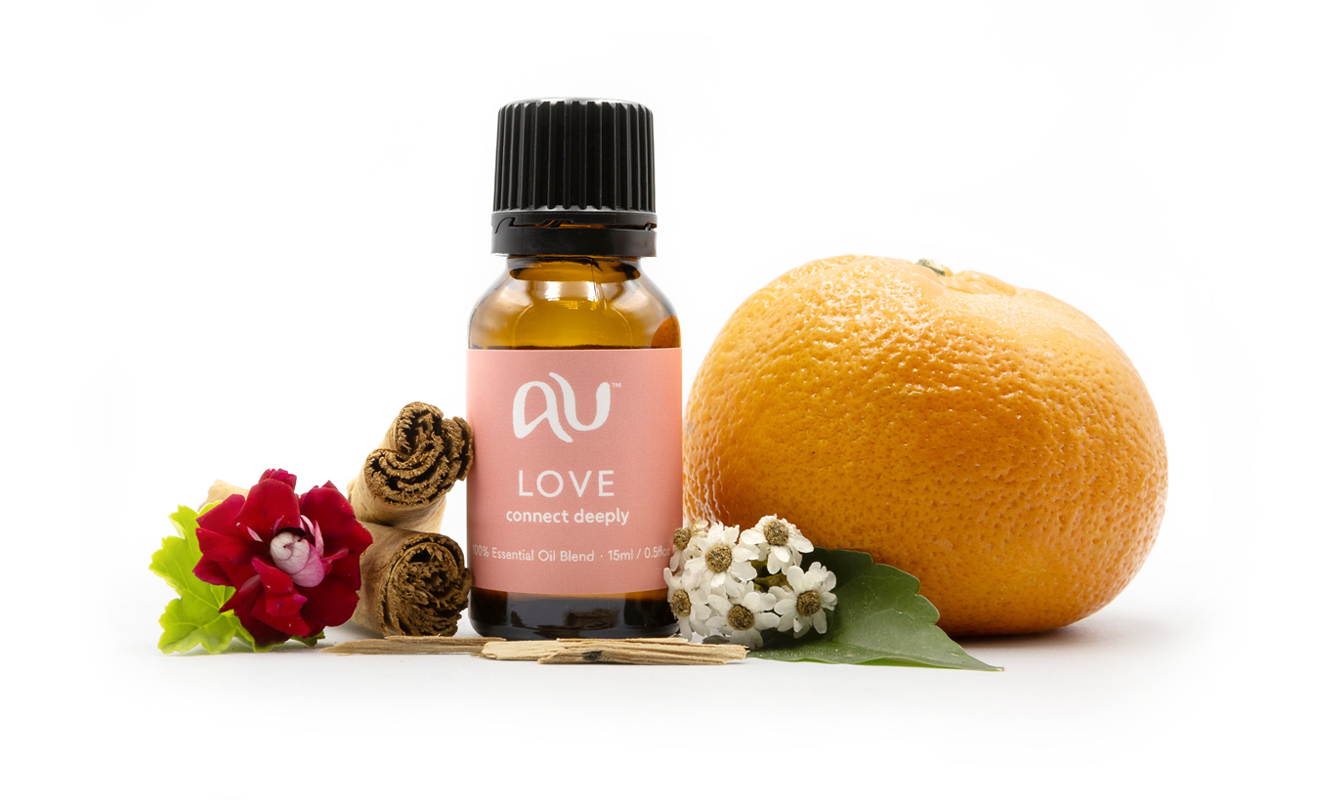 The Love Essential Oil Blend bottle is arranged on a white background surrounded by its ingredients - fruit, herbs and spices.