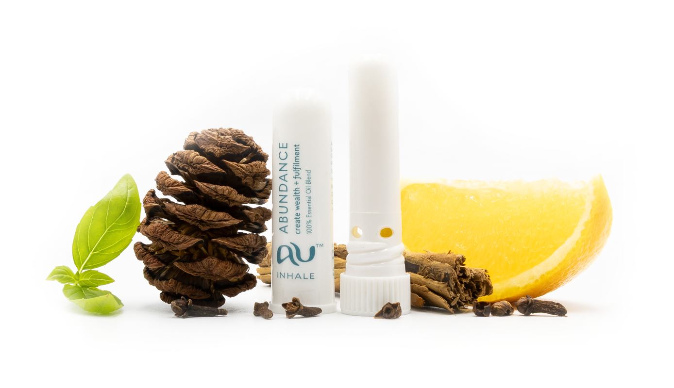 The Abundance Essential Oil inhaler is arranged on a white background, the cap has been taken off and it sitting next to the inhaler, surrounded by its ingredients - fruit, herbs and spices.