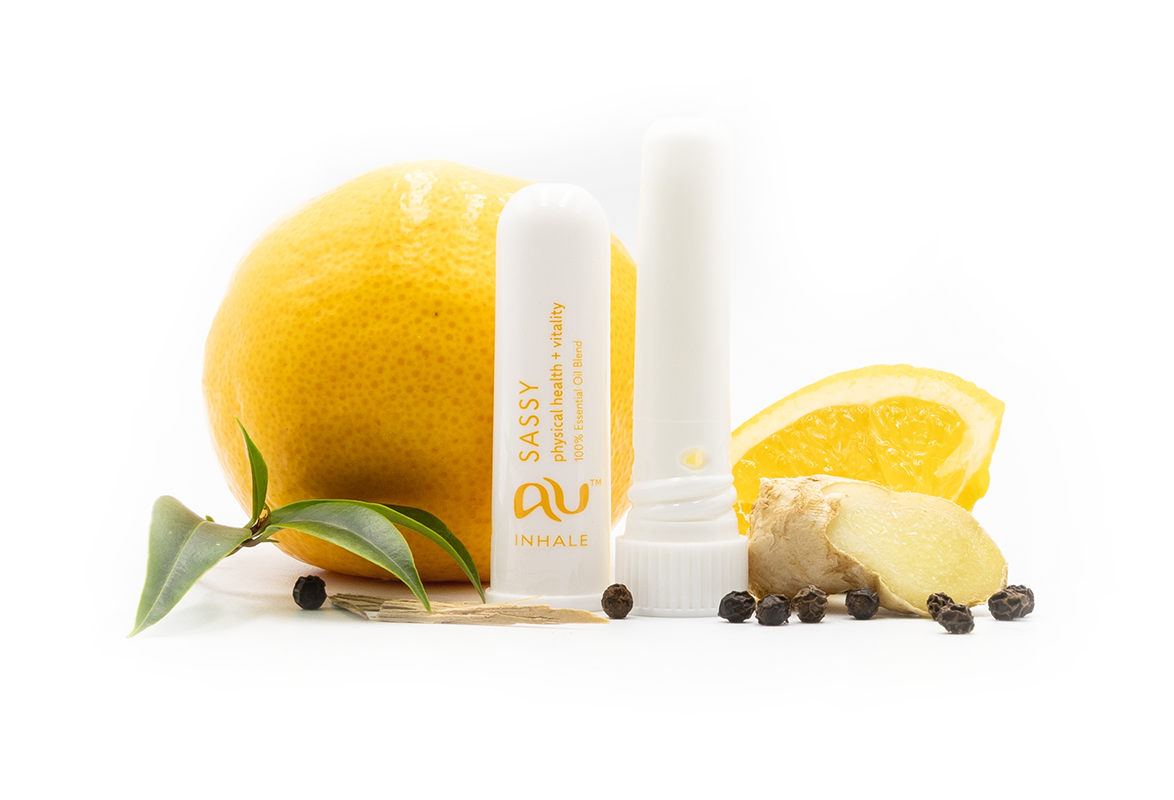 The Sassy Essential Oil inhaler is arranged on a white background, the cap has been taken off and it sitting next to the inhaler, surrounded by its ingredients - fruit, herbs and spices.