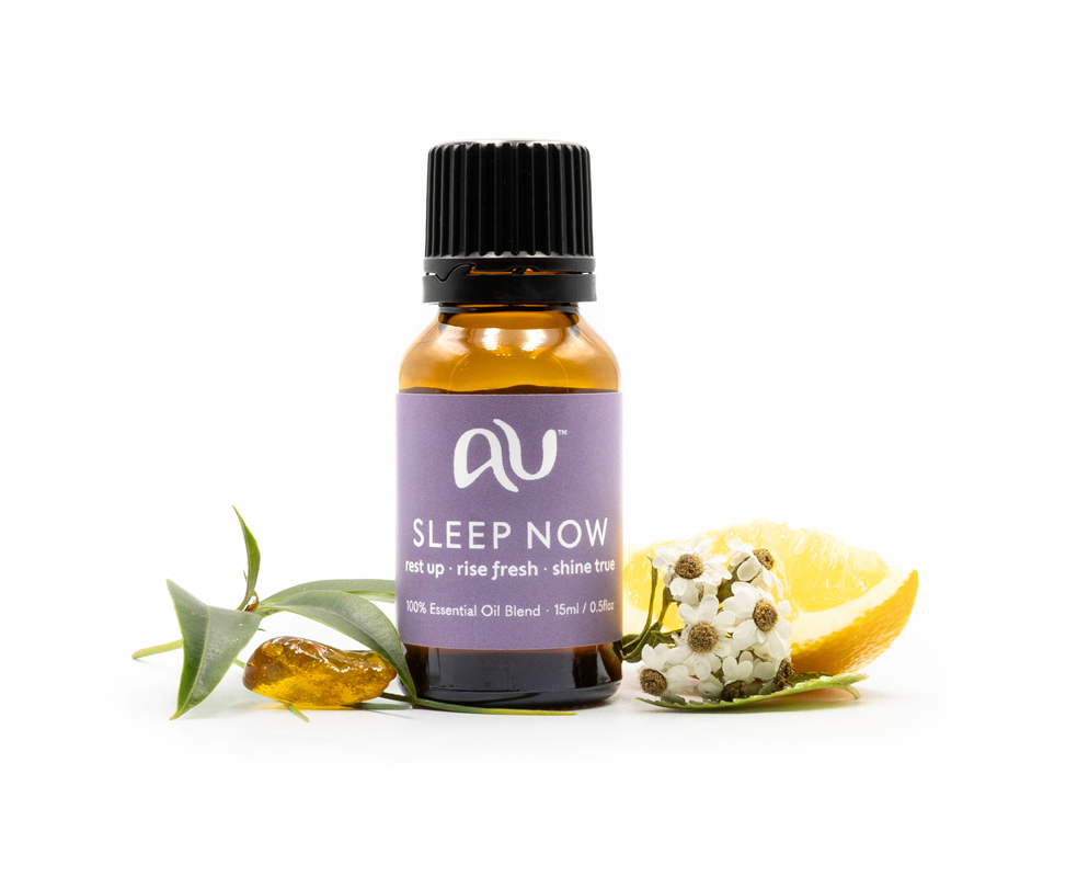 The Sleep Now Essential Oil Blend bottle is arranged on a white background surrounded by its ingredients - fruit, herbs and spices.