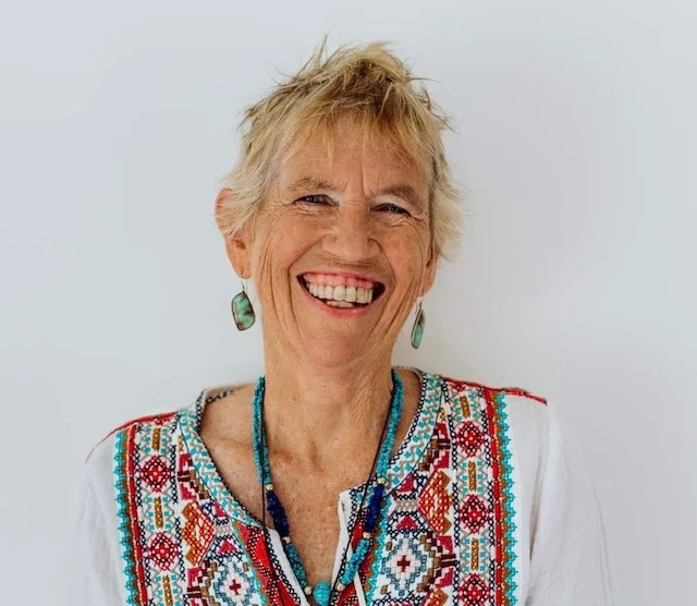 Smiling Sali McIntyre with short, blonde hair, wearing turquoise earrings and a colourful embroidered blouse.