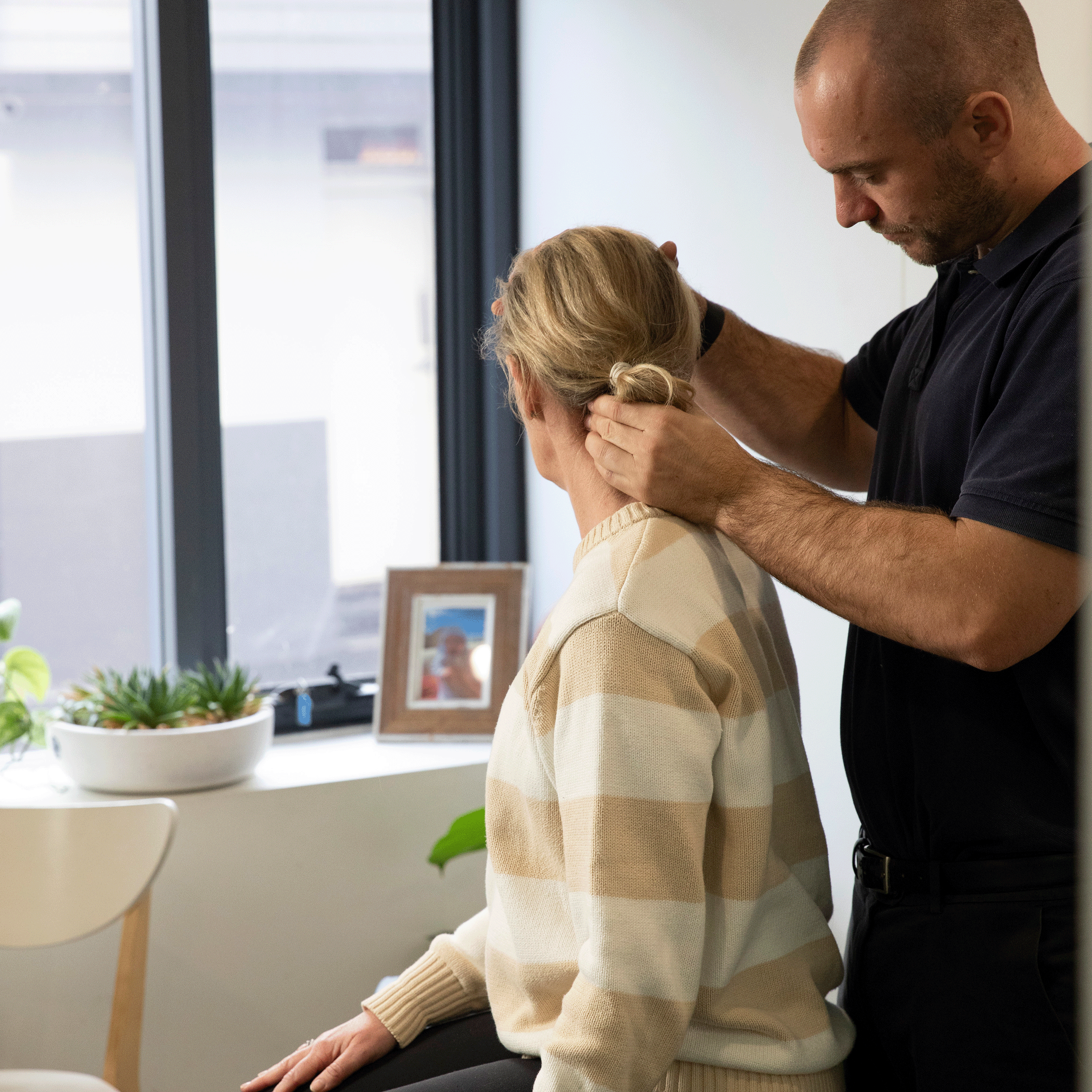 Chiropractic practitioner helping a client stretch her neck while they are sitting up on a treatment table