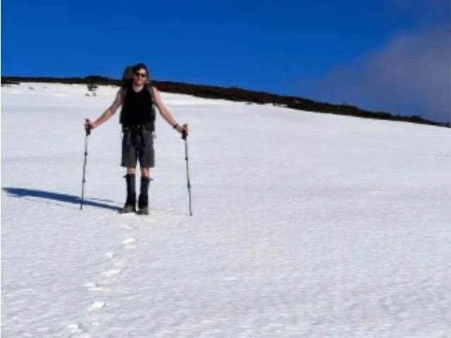 Person hiking in snow with trekking poles on a sunny day.