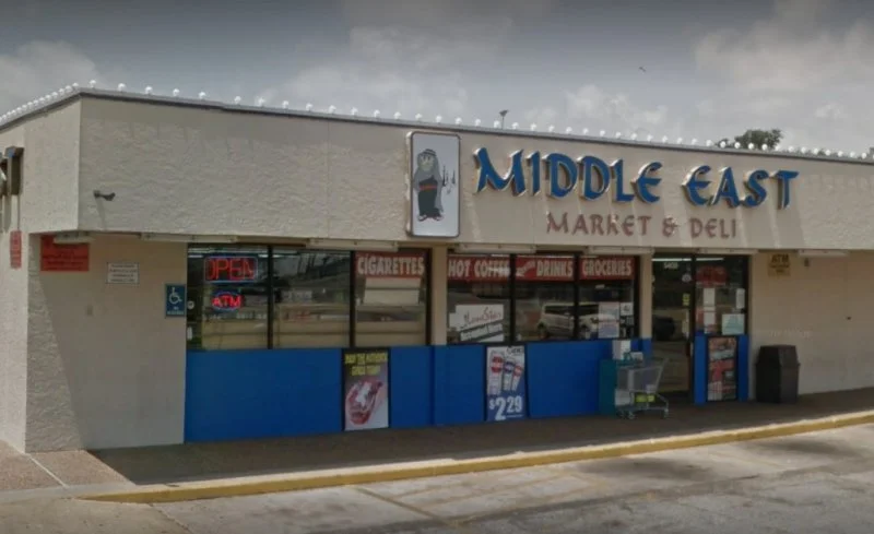 Facade of Middle East Market & Deli with signage, shop windows displaying advertisements, and a handicapped parking space.