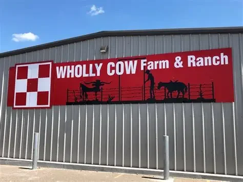 Sign for Wholly Cow Farm & Ranch featuring barnyard silhouettes of cows, a person, and a chicken on a red background.