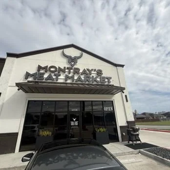 The exterior of Montray's Meat Market storefront with a bull head logo, large glass doors, and an open sign. The sky is partly cloudy.