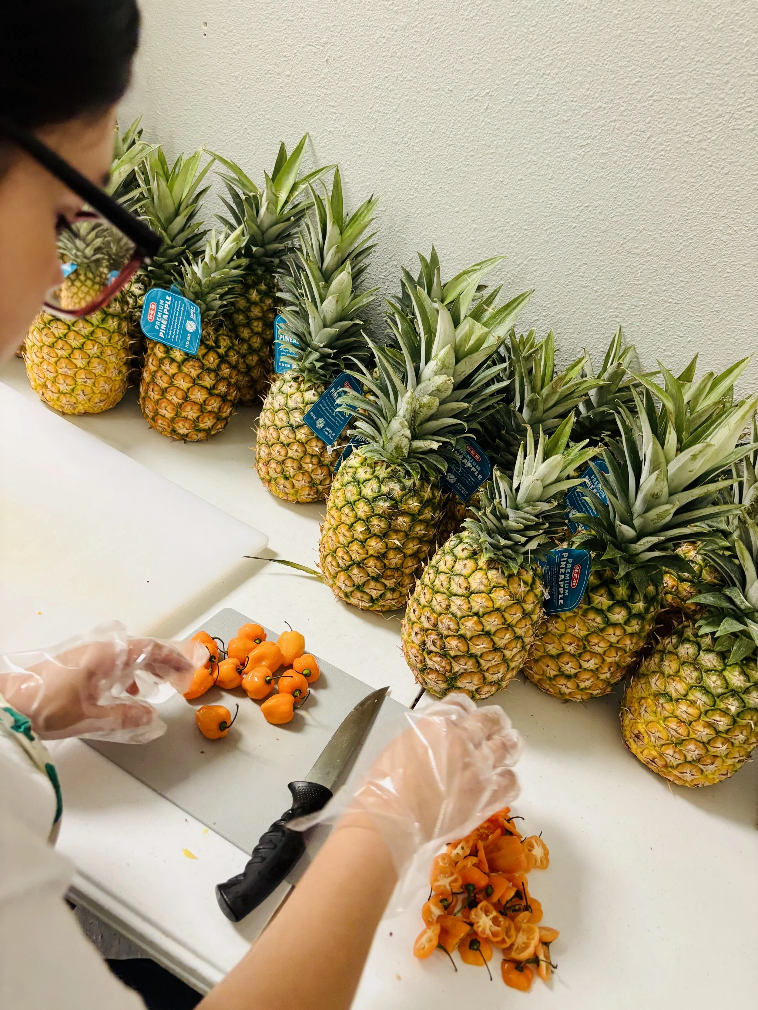 Person slicing orange peppers in a kitchen with a row of pineapples on a counter behind them.