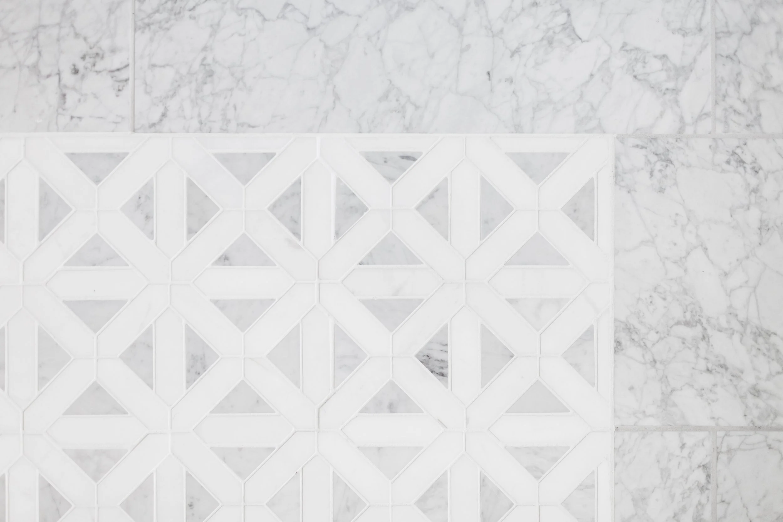 Close-up view of a decorative white tile with a geometric lattice pattern, surrounded by grey and white marble tiles.