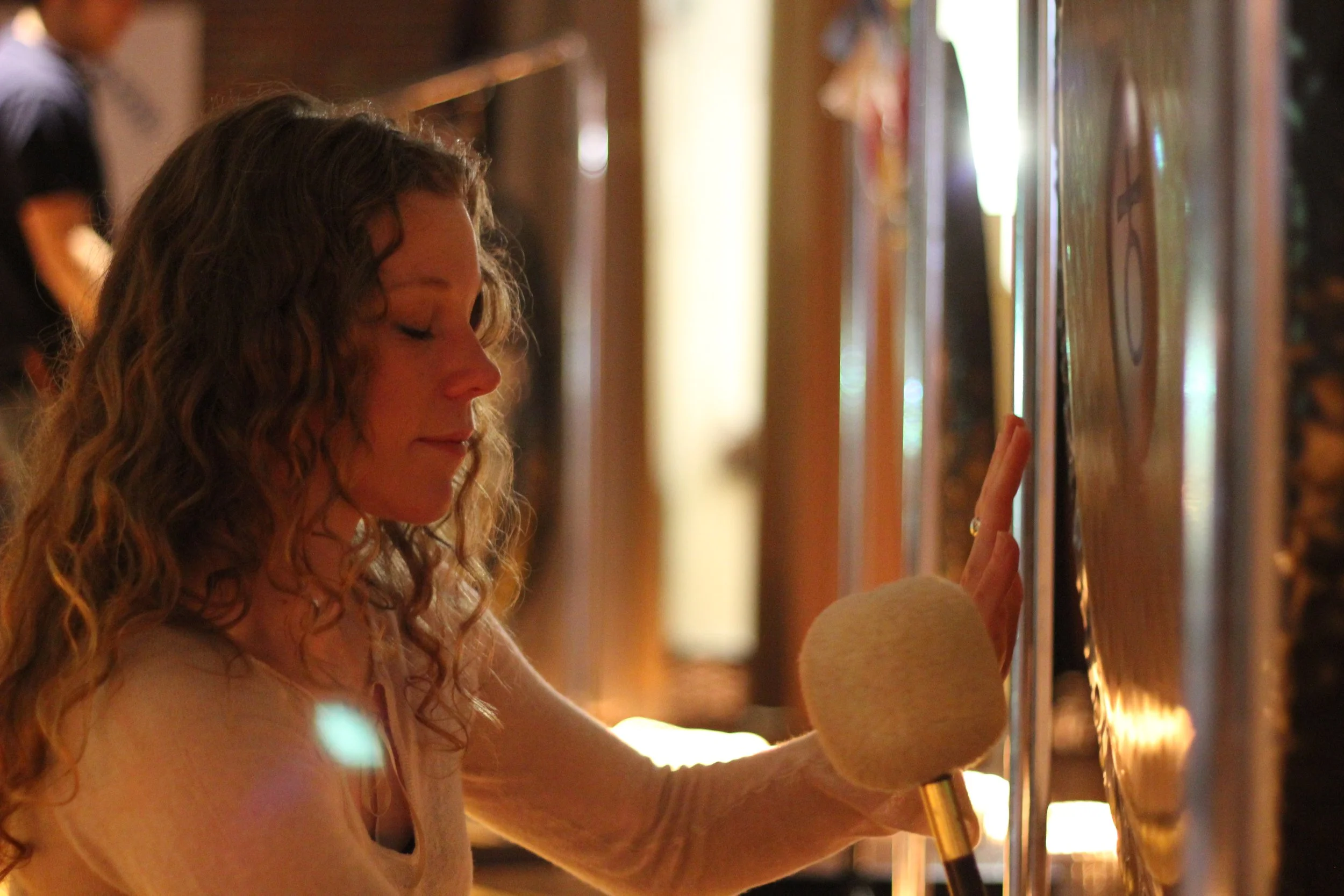 A woman with long curly hair touching a display on a wall with her hand in a softly lit room.