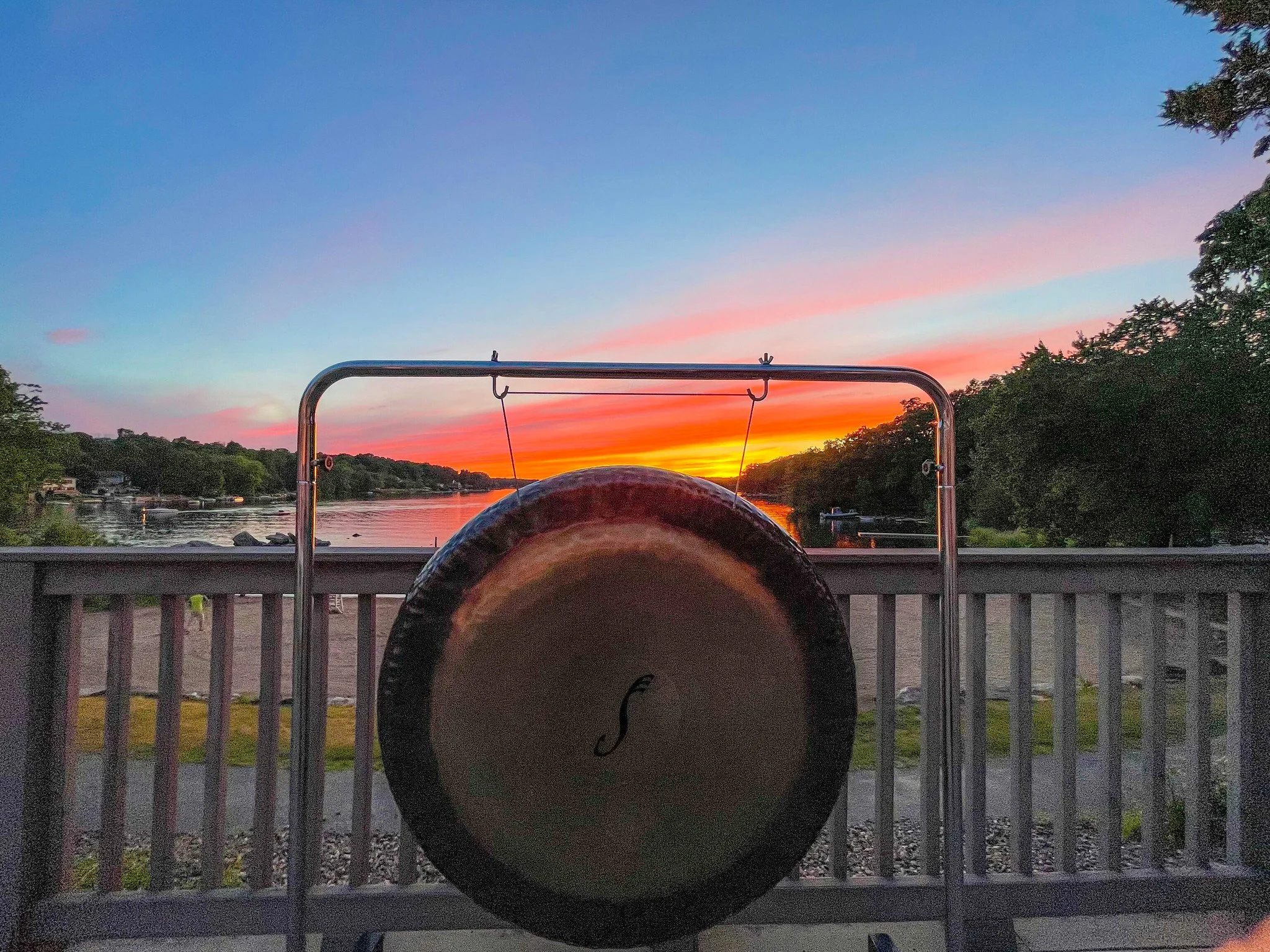 Gong hanging on a stand on a balcony overlooking a Lake Wangumbaug, better known as Coventry Lake at sunset with colorful sky.
