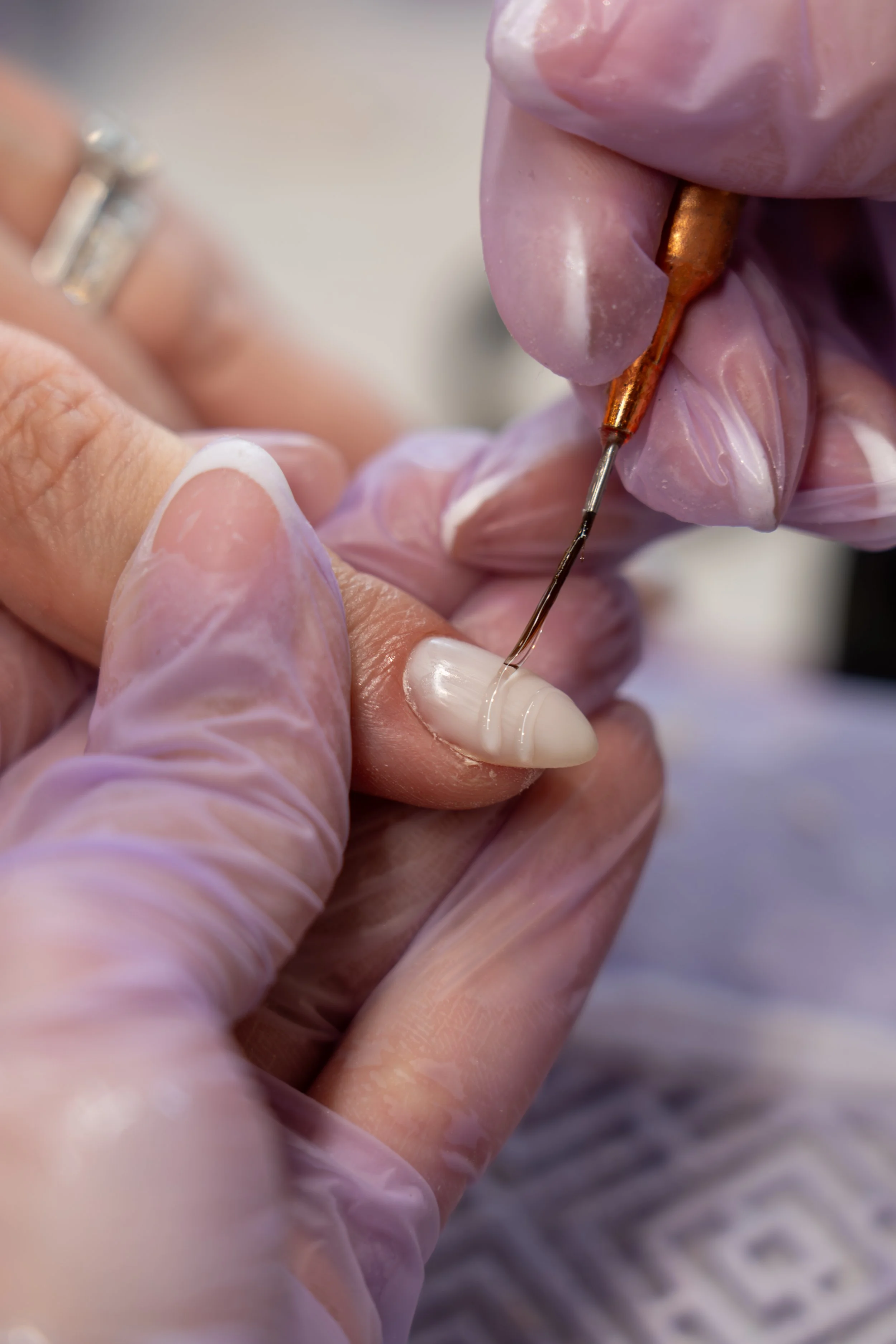 Dental professional wearing pink gloves applying nail primer on a patient's fingernail with a small brush.